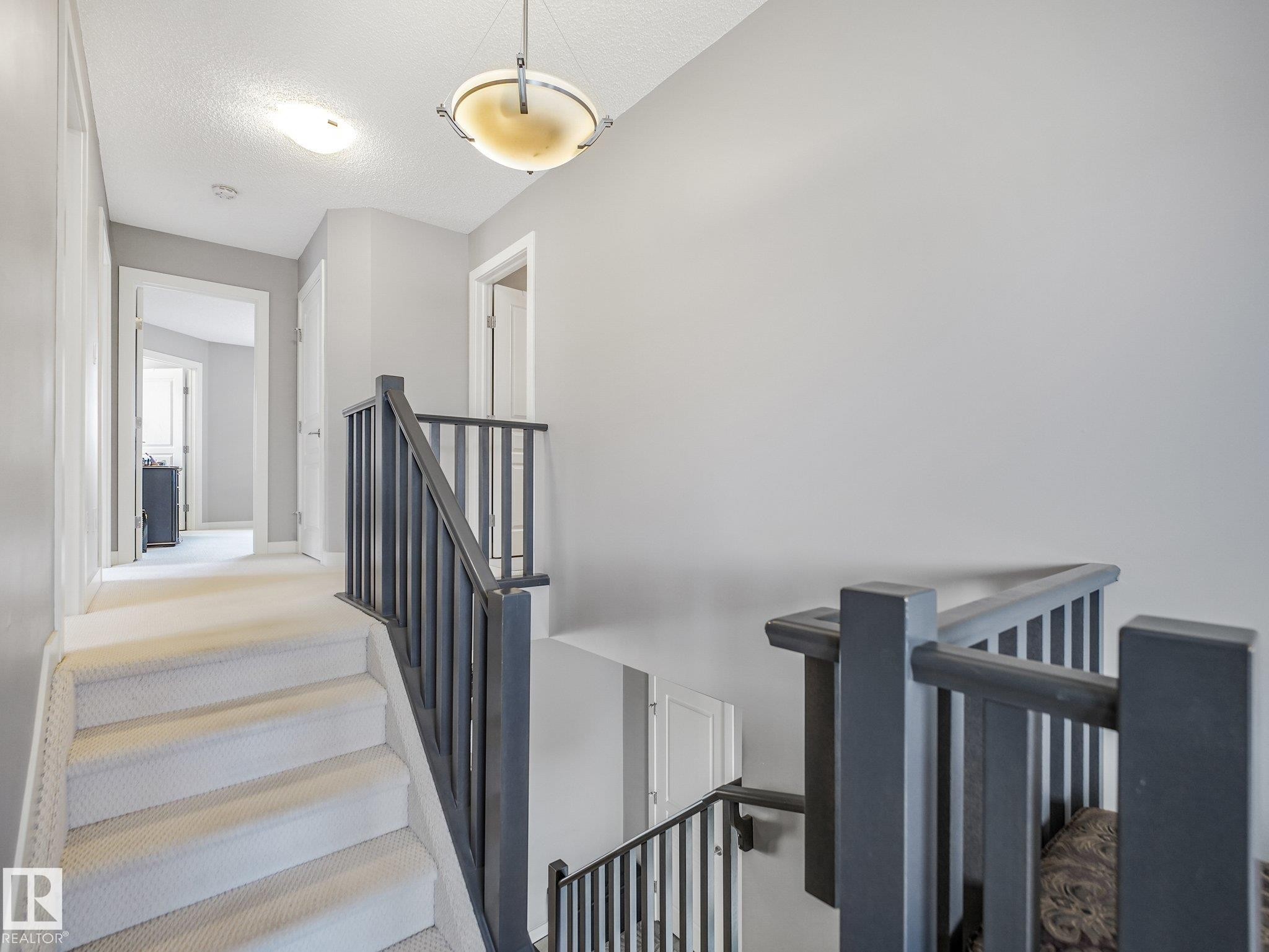 Upper hallway featuring a carpeted staircase, dark wood banister, and a semi-flush mount ceiling fixture - 1478 37B Avenue Nw, Edmonton, AB - Indoor Photo Showing Other Room