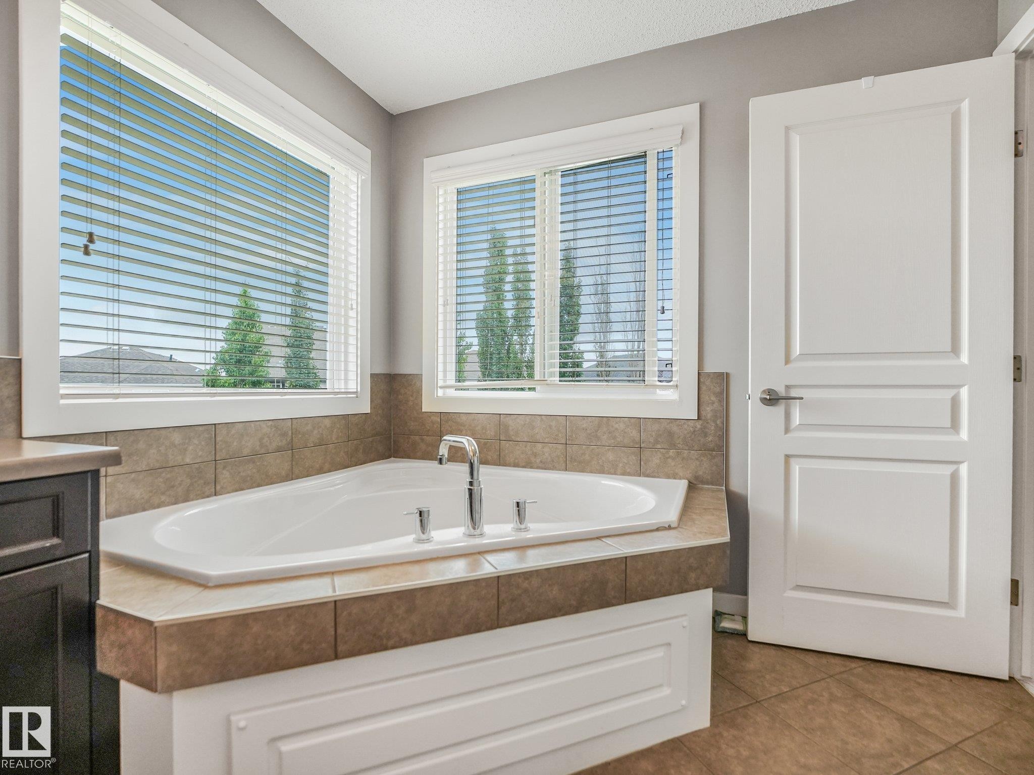 Corner soaking tub with tile surround, dual windows, and built-in cabinetry - 1478 37B Avenue Nw, Edmonton, AB - Indoor Photo Showing Bathroom