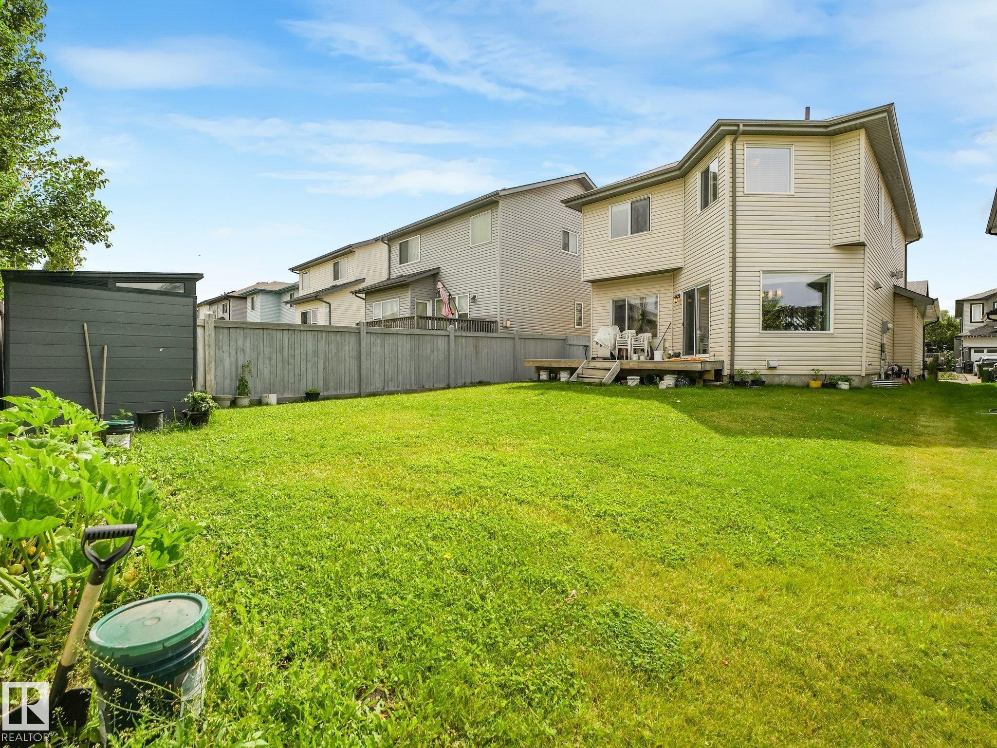 Expansive lawn area with a wood privacy fence, a modern storage shed, and a raised wood deck - 1478 37B Avenue Nw, Edmonton, AB - Outdoor