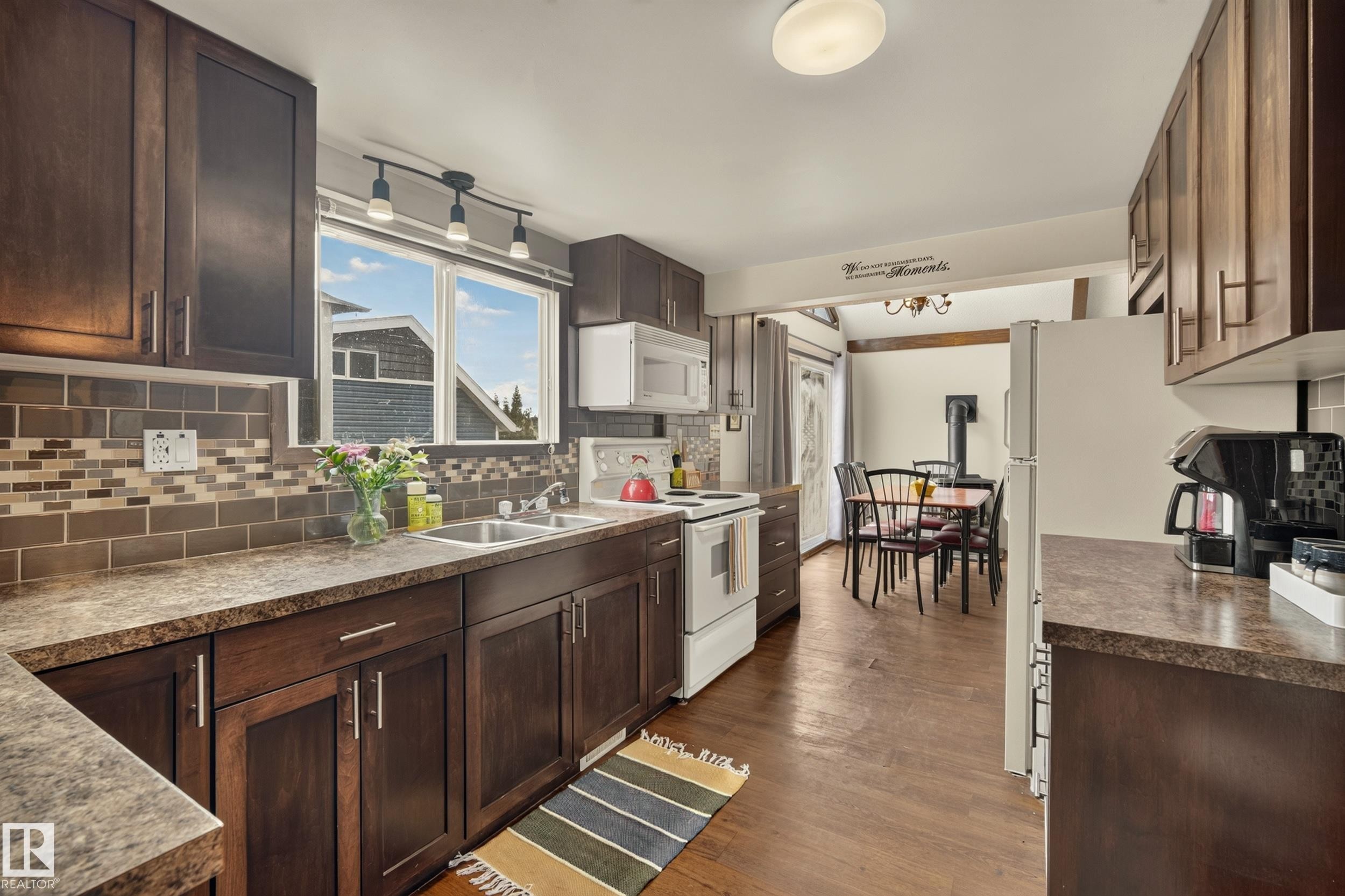 Kitchen featuring dark wood-finish cabinetry, a subway tile backsplash with mosaic accents, and a dual-basin stainless steel sink - 264 Beach Avenue, Rural Barrhead County, AB - Indoor Photo Showing Kitchen With Double Sink