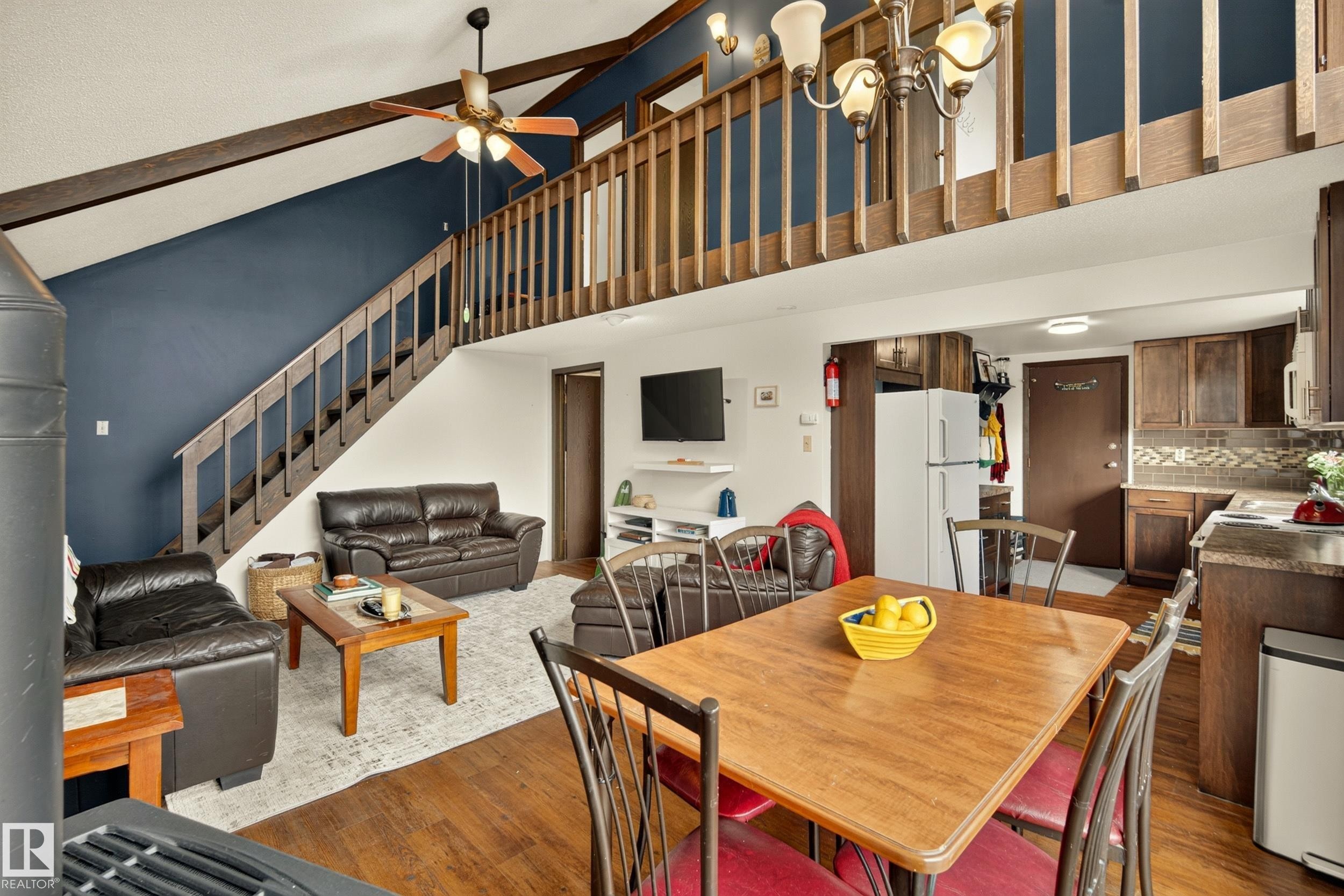 Vaulted ceiling with exposed beams, wood-finish flooring, staircase to upper level, and a kitchen with wood cabinetry and tile backsplash - 264 Beach Avenue, Rural Barrhead County, AB - Indoor