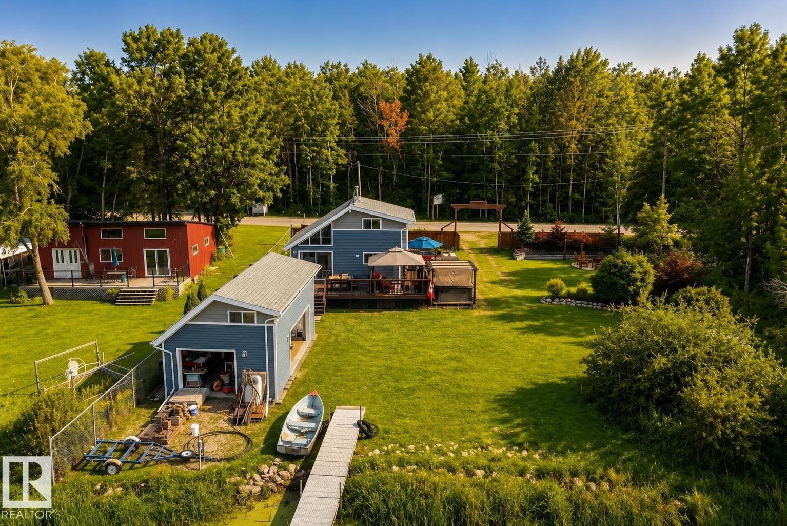 Expansive green lawn, waterfront access with a dock, two distinct structures with decks, a detached garage, and mature tree-lined surroundings - 264 Beach Avenue, Rural Barrhead County, AB - Outdoor