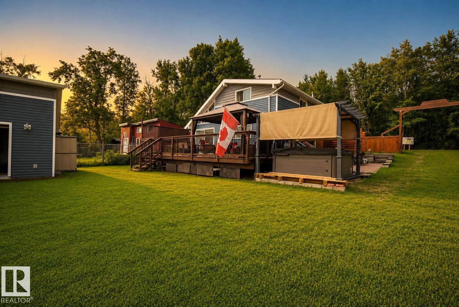 Expansive green lawn, multi-level wood deck, outdoor hot tub with canopy, stone patio, and detached building with siding - 264 Beach Avenue, Rural Barrhead County, AB - Outdoor With Deck Patio Veranda