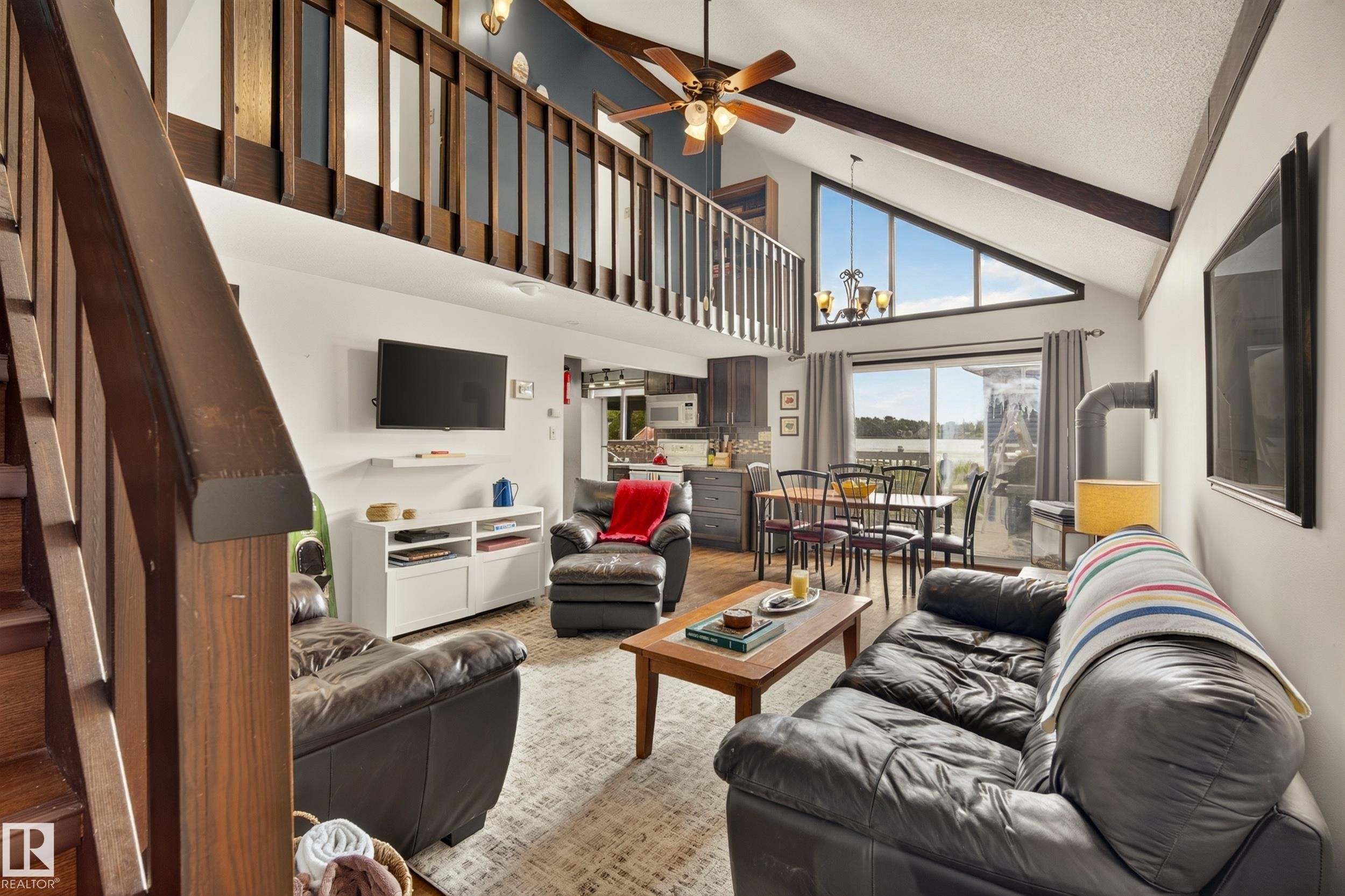Vaulted ceiling with exposed beams, lofted interior balcony, large triangular window, sliding glass door, and wood-finish flooring - 264 Beach Avenue, Rural Barrhead County, AB - Indoor