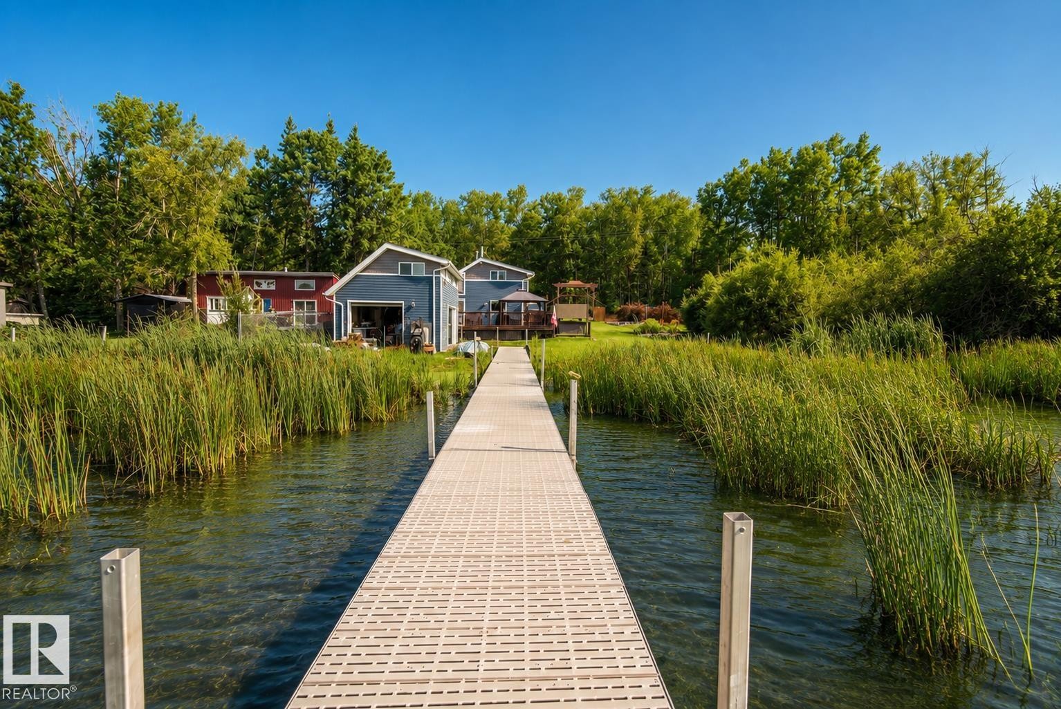 Dock extending into a body of water, surrounded by tall reeds, mature trees, and a clear blue sky - 264 Beach Avenue, Rural Barrhead County, AB - Outdoor With Body Of Water