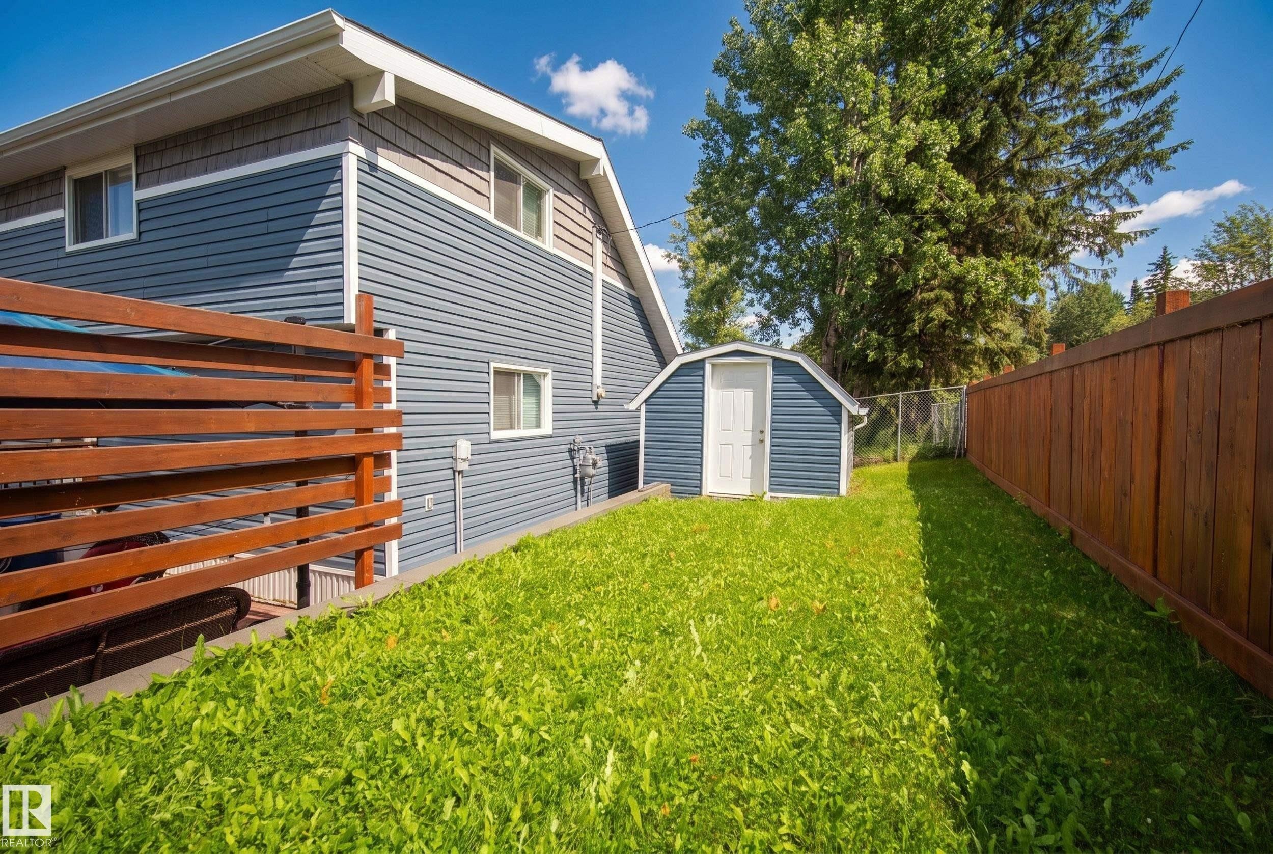 Expansive grass lawn with a wood-slatted fence, a privacy fence, and a storage shed - 264 Beach Avenue, Rural Barrhead County, AB - Outdoor