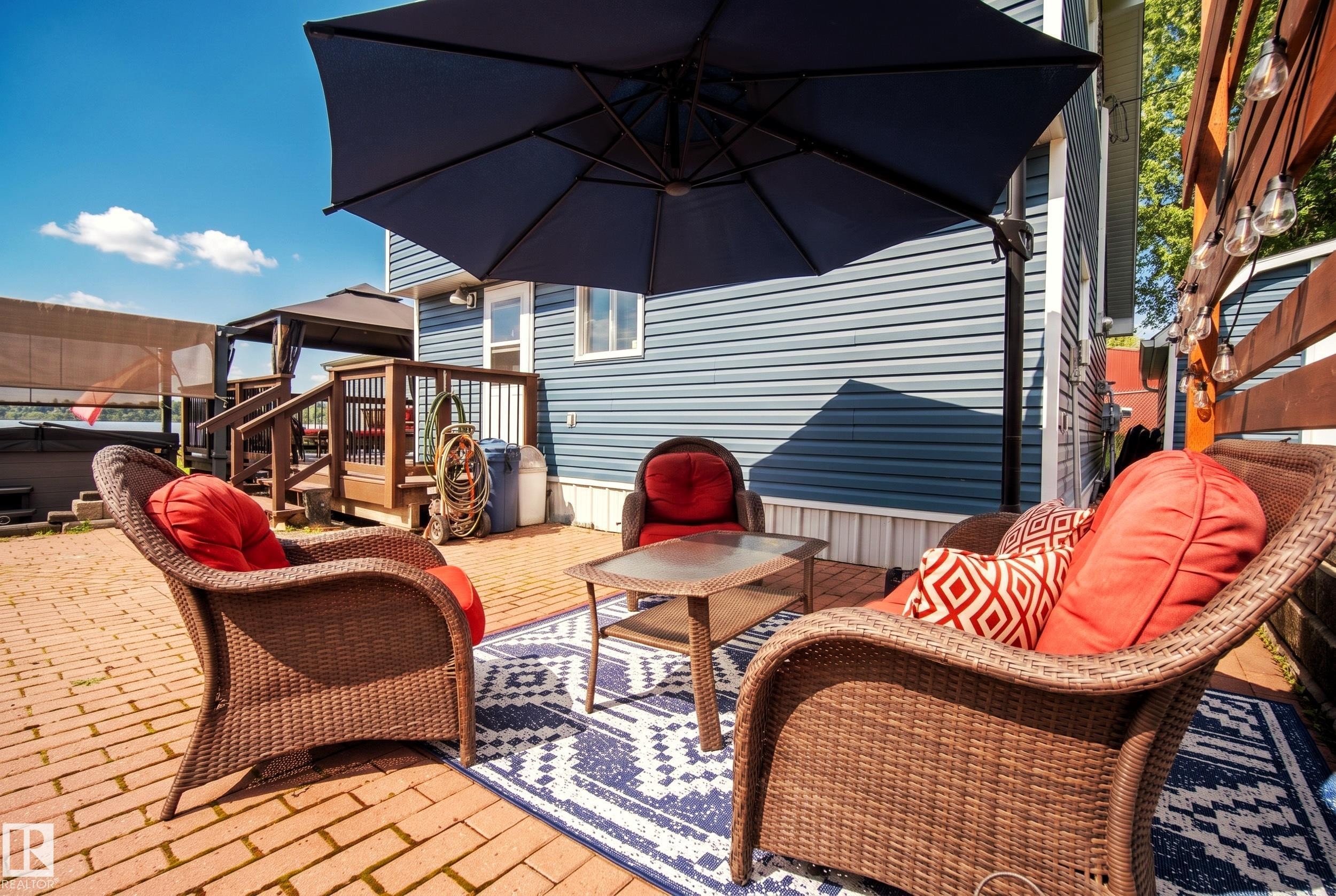 Brick paver patio with a decorative area rug and adjacent wood-built deck - 264 Beach Avenue, Rural Barrhead County, AB - Outdoor With Deck Patio Veranda With Exterior