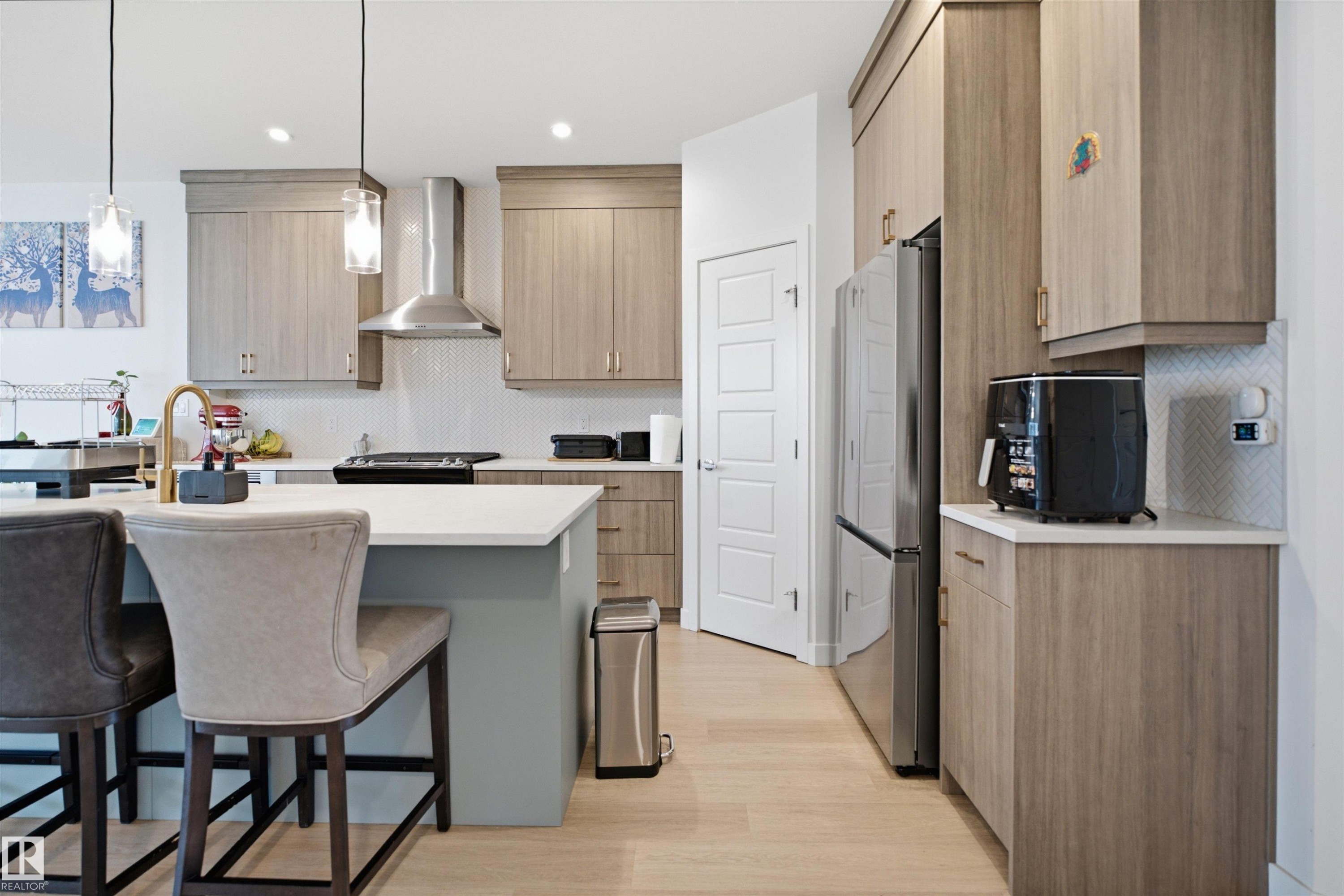Modern kitchen featuring wood-finish cabinetry, stainless steel appliances, white countertops, and light wood-finish flooring - 3877 Chrustawka Place Sw, Edmonton, AB - Indoor Photo Showing Other Room