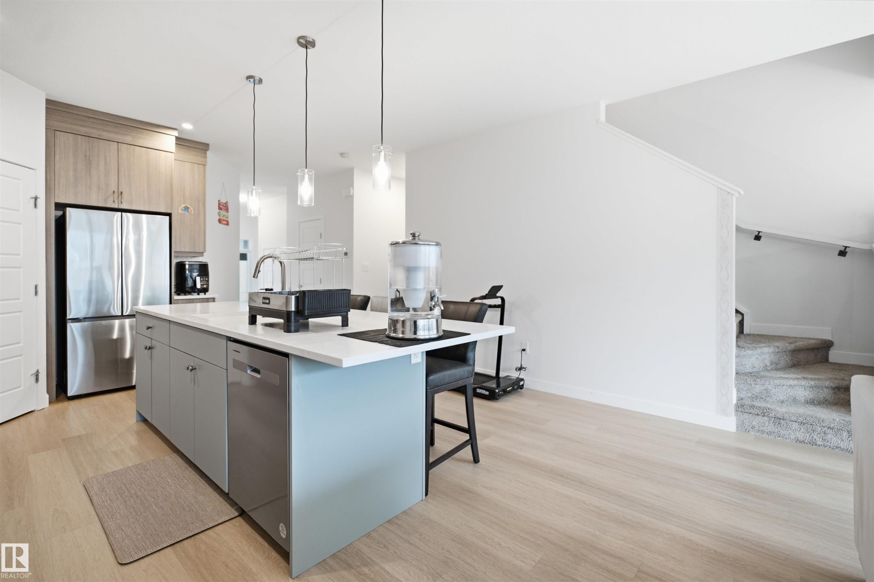 Kitchen island with a light-toned countertop, pendant lighting, stainless steel appliances, and wood-finish flooring - 3877 Chrustawka Place Sw, Edmonton, AB - Indoor Photo Showing Kitchen With Upgraded Kitchen