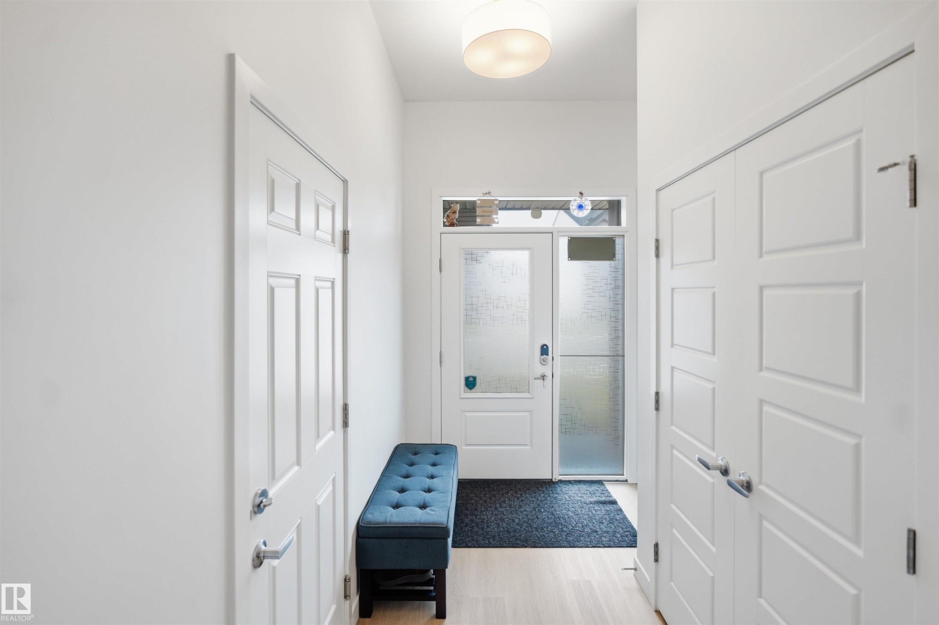 Entryway featuring a panel door, frosted glass sidelight, wood-finish flooring, and a modern flush-mount light fixture - 3877 Chrustawka Place Sw, Edmonton, AB - Indoor Photo Showing Other Room