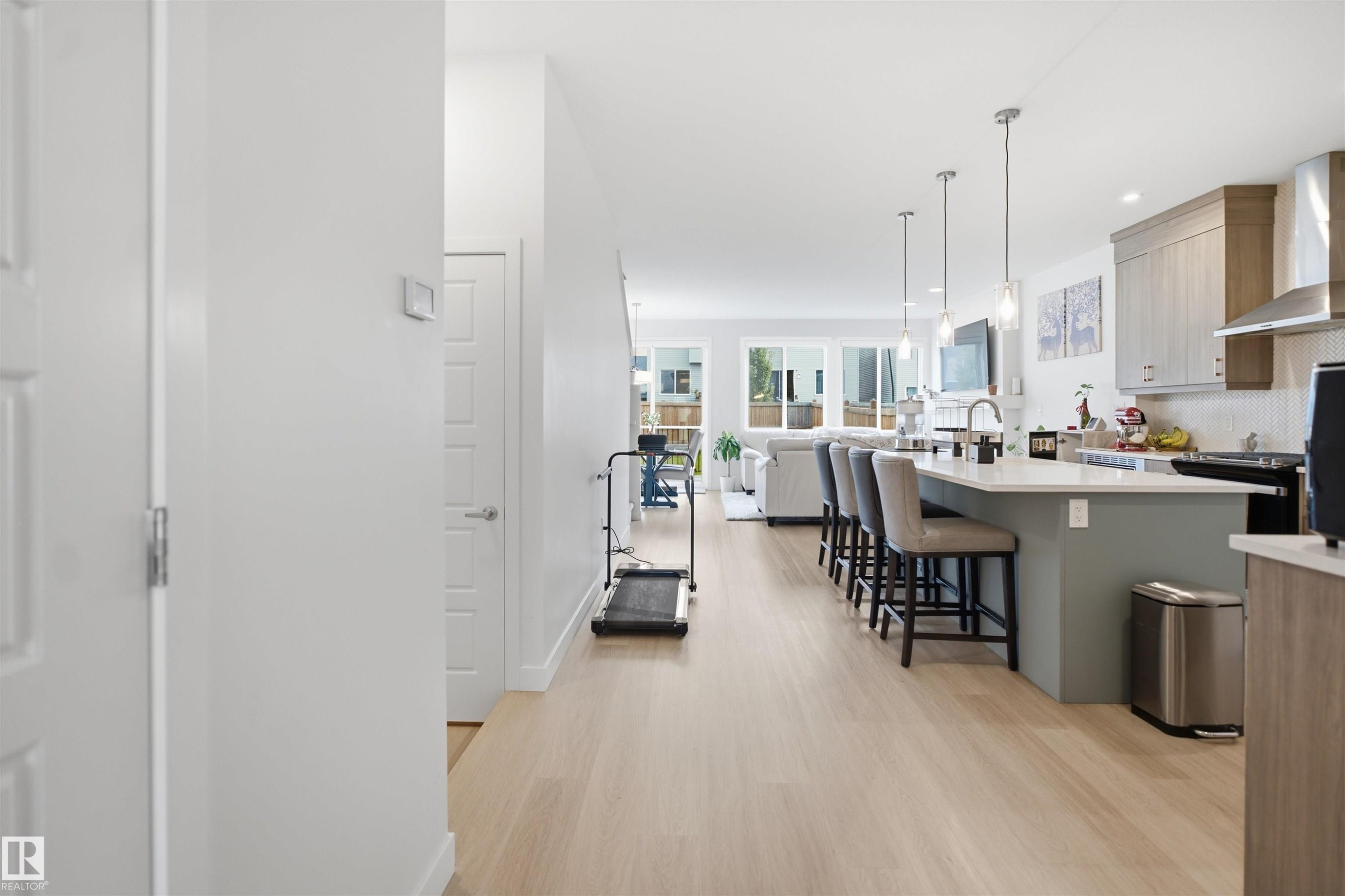 Wood-finish flooring throughout, kitchen island with seating, stainless steel appliances, modern pendant lighting, and recessed overhead lighting - 3877 Chrustawka Place Sw, Edmonton, AB - Indoor Photo Showing Kitchen With Upgraded Kitchen