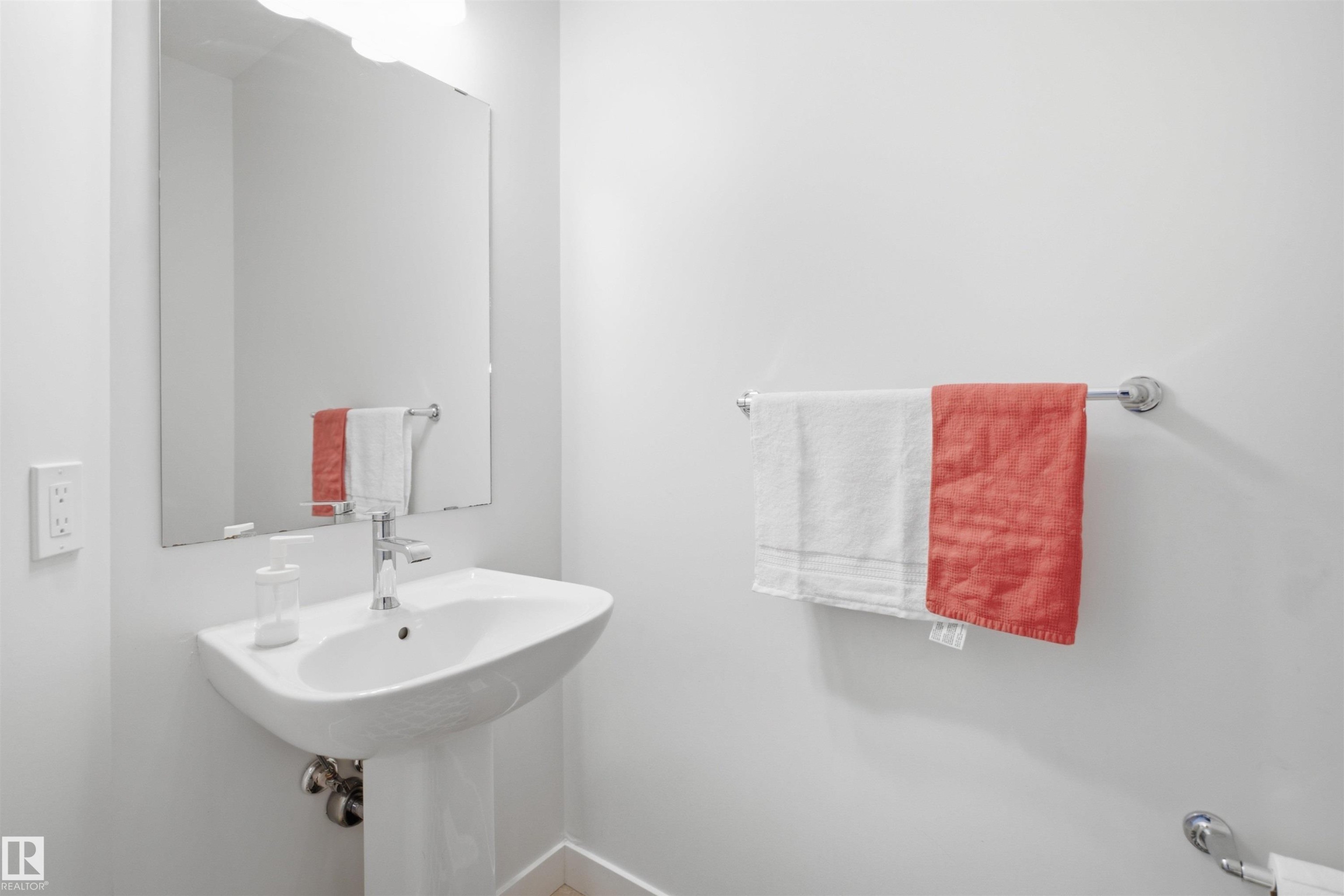 Pedestal sink with a polished chrome faucet, rectangular wall mirror, and wall-mounted light fixture - 3877 Chrustawka Place Sw, Edmonton, AB - Indoor Photo Showing Bathroom
