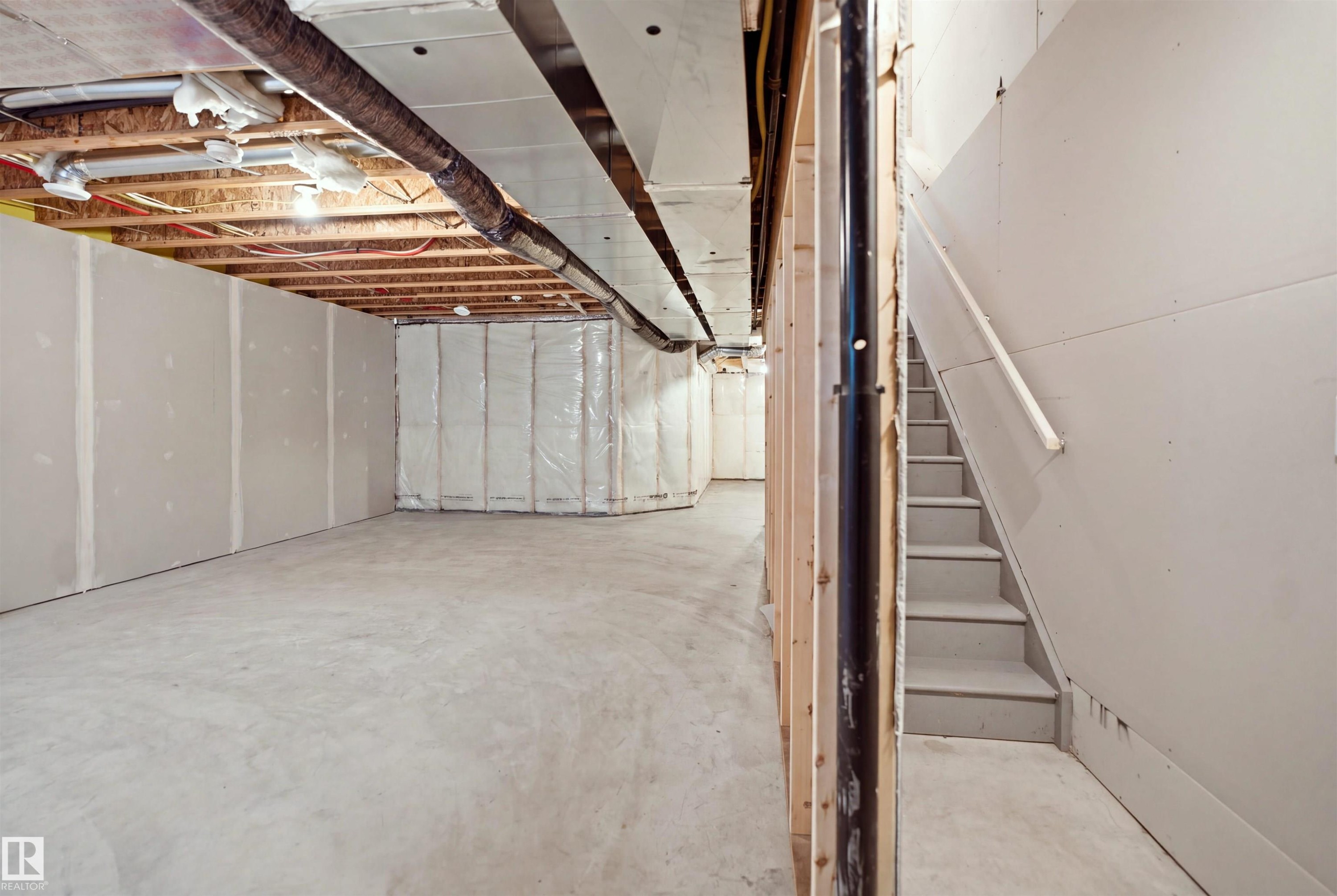 Unfinished basement with exposed ceiling joists, concrete flooring, insulated walls, and a staircase with a handrail - 3877 Chrustawka Place Sw, Edmonton, AB - Indoor Photo Showing Basement