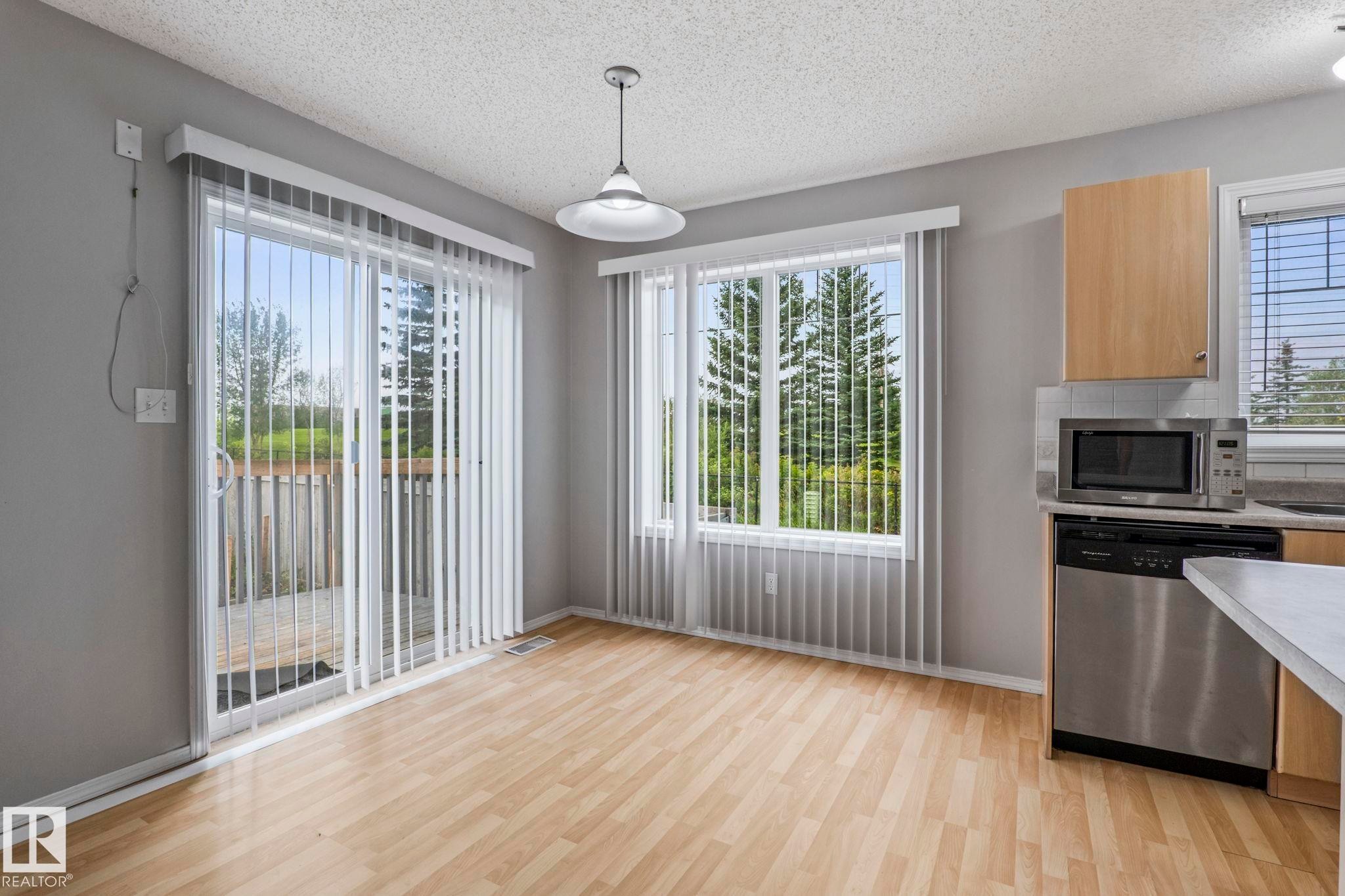 Sliding glass door to an outdoor deck, wood-finish flooring, ample natural light, stainless steel dishwasher, and built-in microwave - #80 4350 23St Nw, Edmonton, AB - Indoor Photo Showing Kitchen