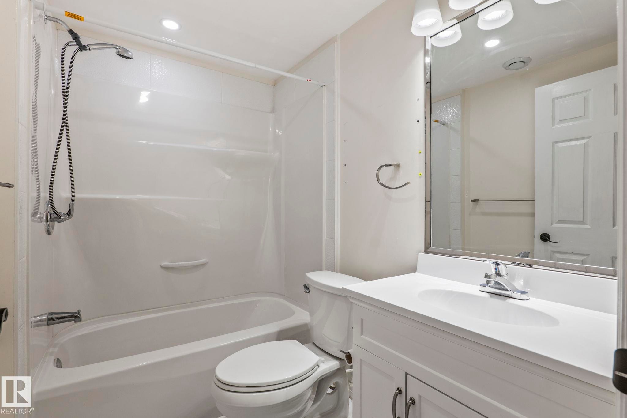Bathtub with an integrated shower, white vanity with a single basin sink, and a framed mirror - #80 4350 23St Nw, Edmonton, AB - Indoor Photo Showing Bathroom