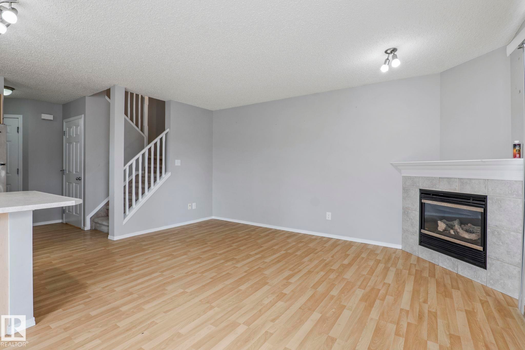 Wood-finish flooring throughout, featuring a corner fireplace with a tiled surround and mantel - #80 4350 23St Nw, Edmonton, AB - Indoor Photo Showing Living Room With Fireplace