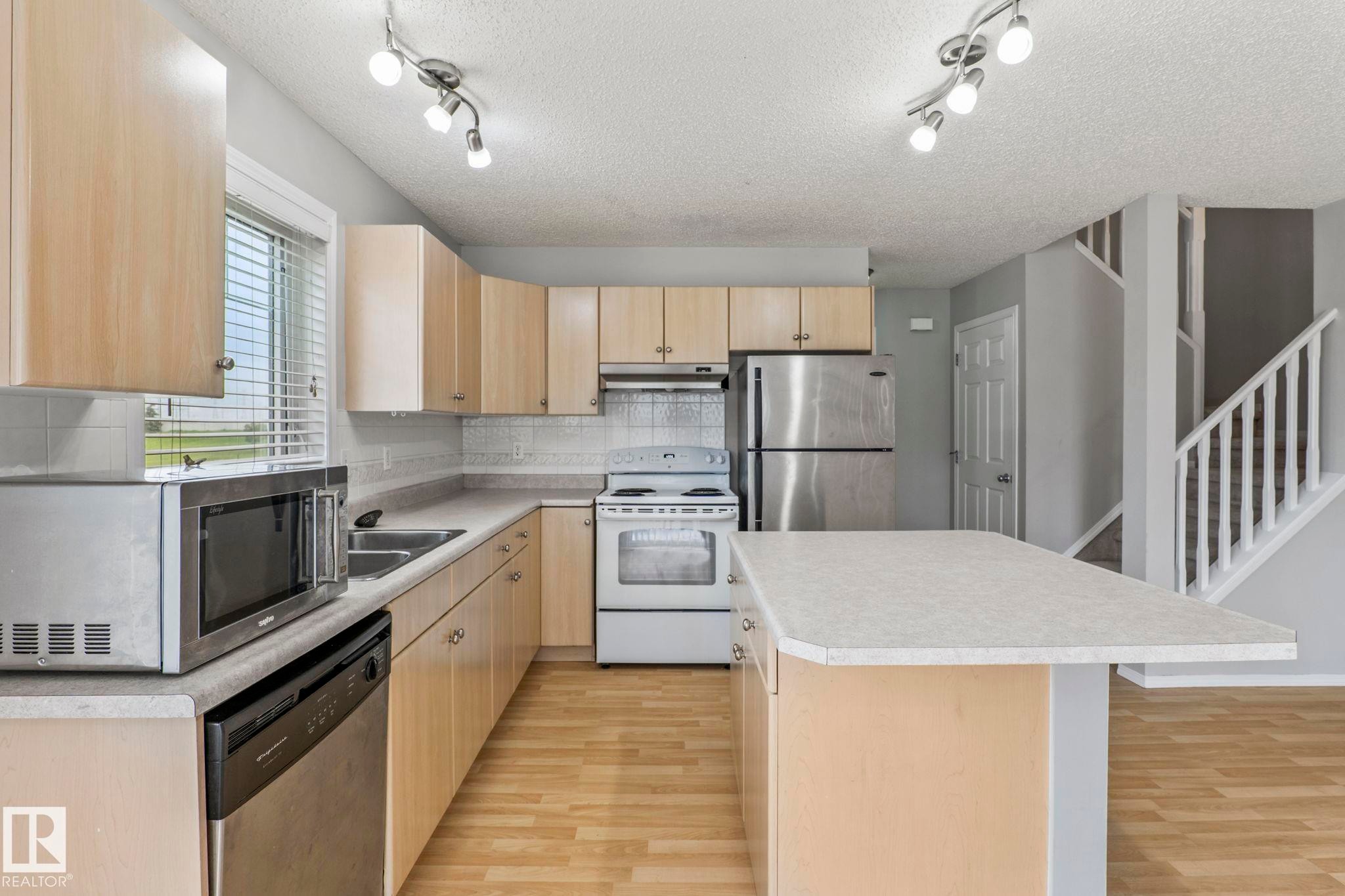 Kitchen featuring light wood-finish cabinetry, light-toned countertops, and a center island - #80 4350 23St Nw, Edmonton, AB - Indoor Photo Showing Kitchen