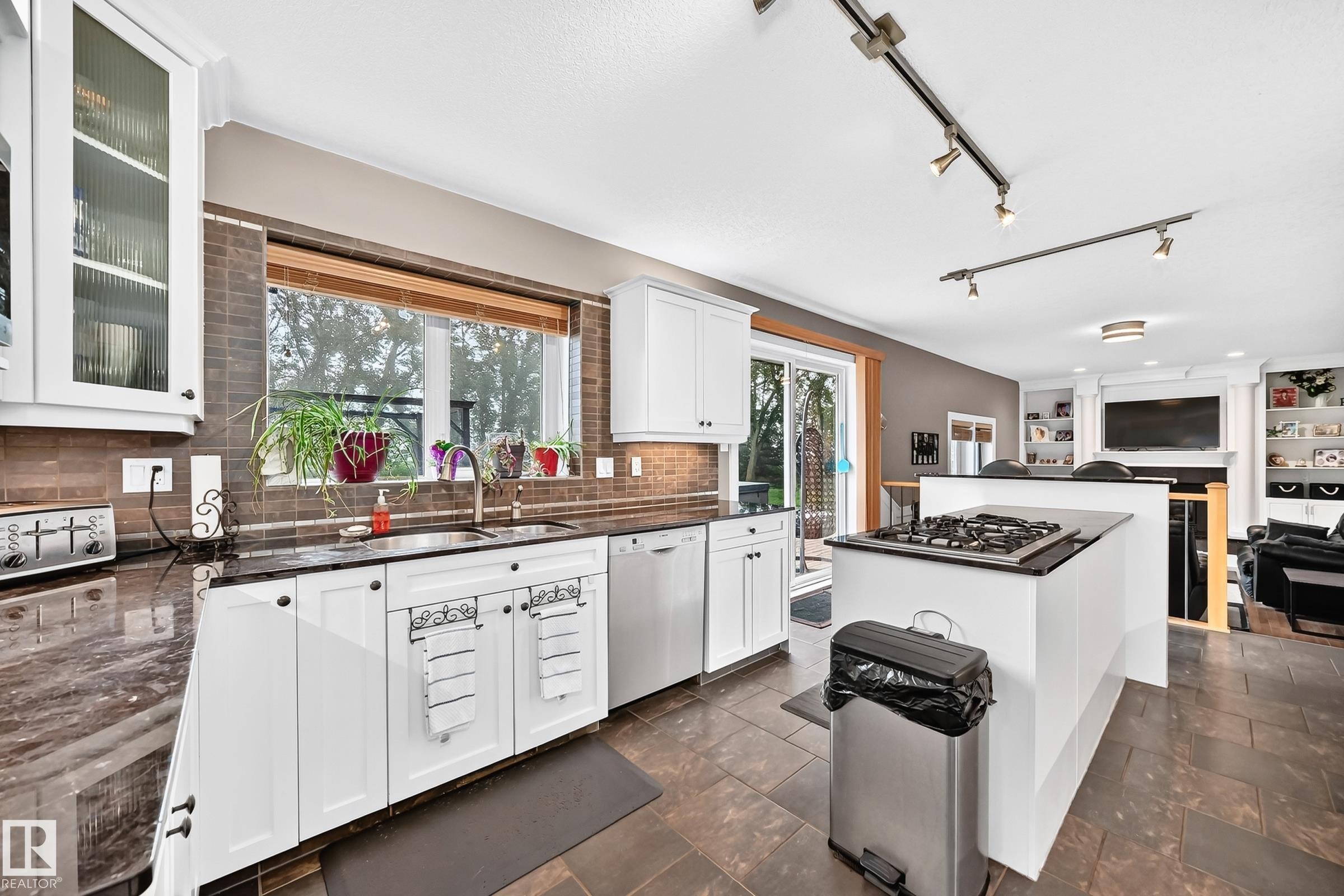 White cabinetry, dark stone countertops, tile backsplash, and stainless steel sink - #38 24512 Sturgeon Rd, Rural Sturgeon County, AB