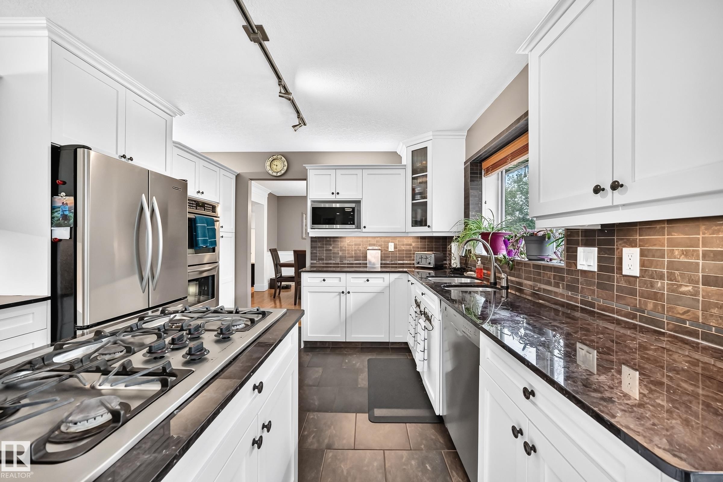 White cabinetry, stainless steel appliances, dark countertops, tiled backsplash, and slate-finish flooring - #38 24512 Sturgeon Rd, Rural Sturgeon County, AB