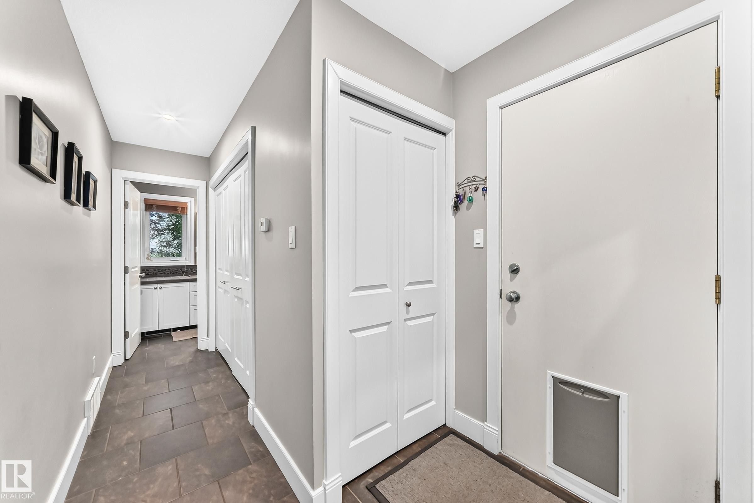 Hallway featuring dark tile flooring, white trim, and a utility room with a built-in vanity and window - #38 24512 Sturgeon Rd, Rural Sturgeon County, AB