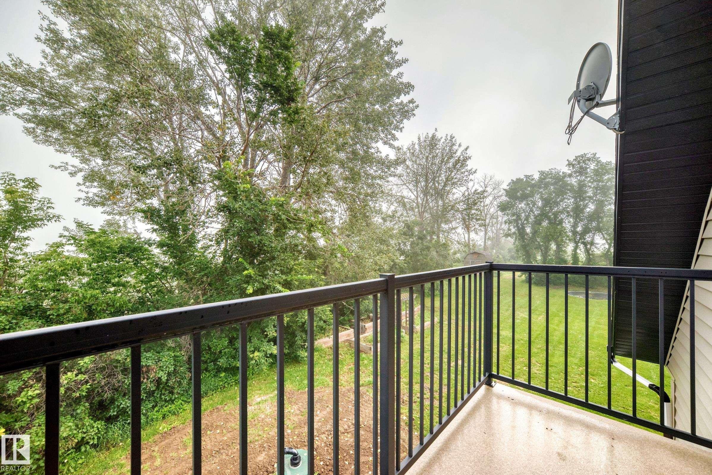 Balcony with black metal railings overlooking mature trees and a grassy area - #38 24512 Sturgeon Rd, Rural Sturgeon County, AB