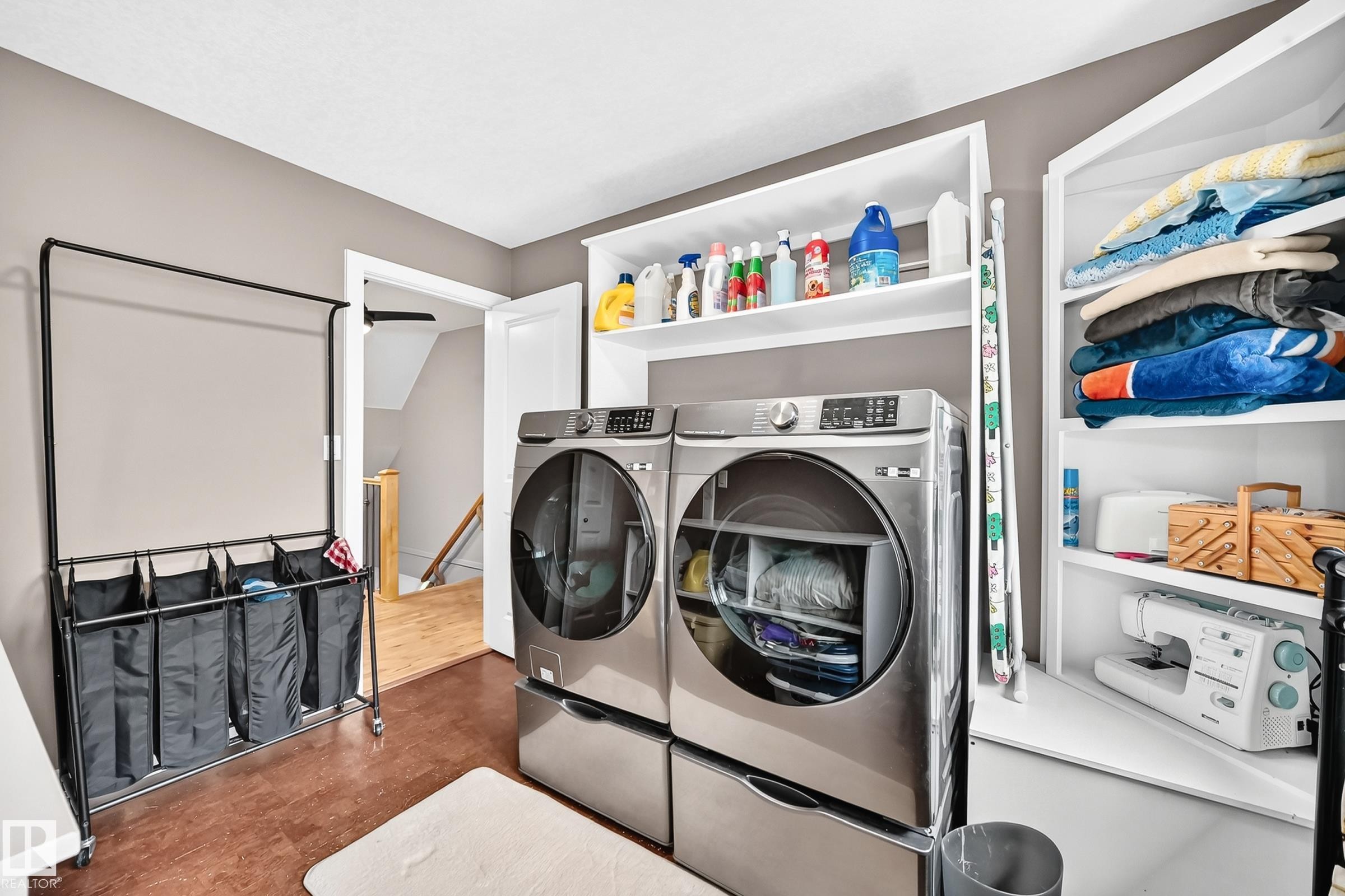 Dedicated laundry area featuring a front-loading washer and dryer, built-in shelving, and wood-finish flooring - #38 24512 Sturgeon Rd, Rural Sturgeon County, AB