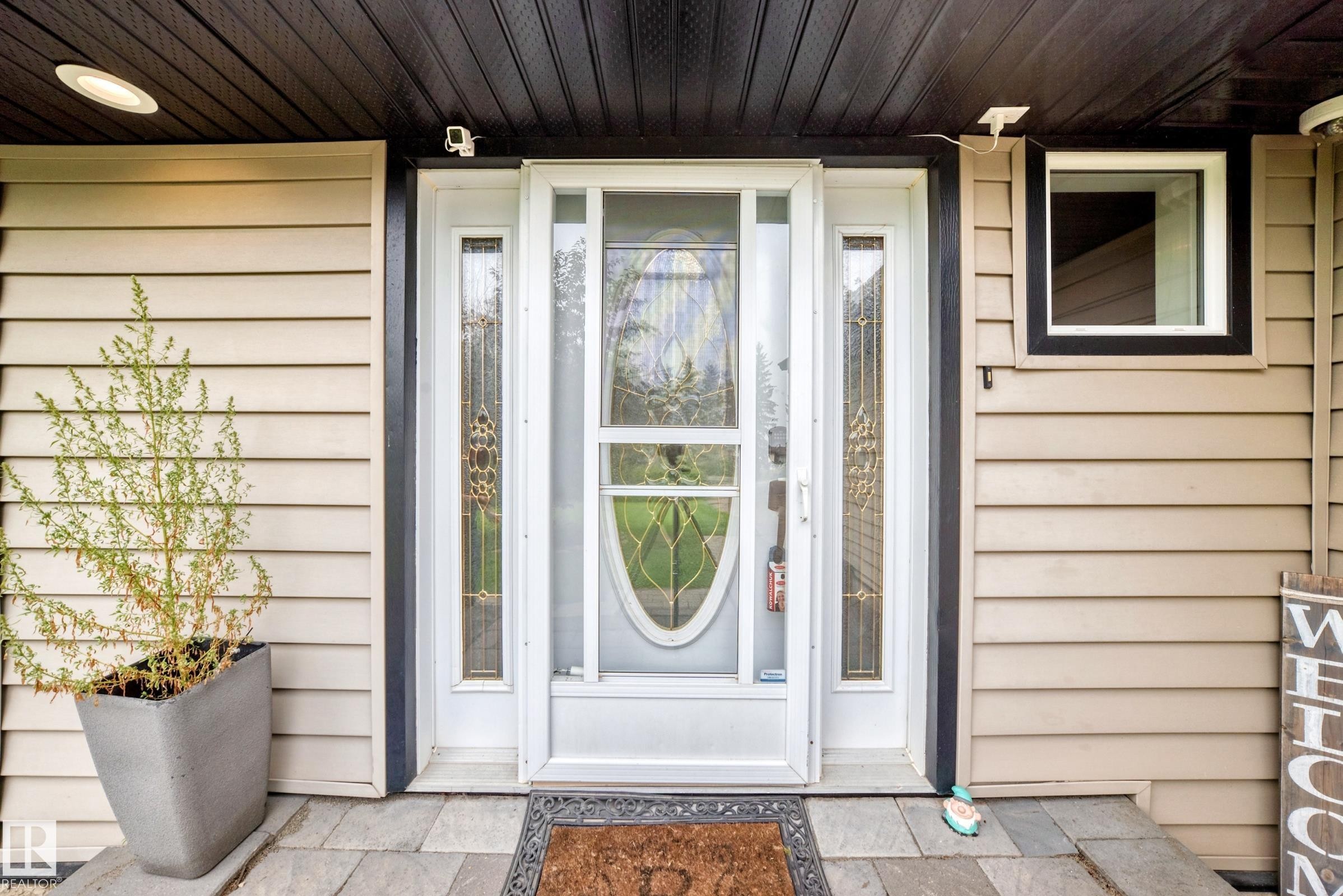 Entryway featuring a white door with decorative glass side panels, black trim, and horizontal siding - #38 24512 Sturgeon Rd, Rural Sturgeon County, AB