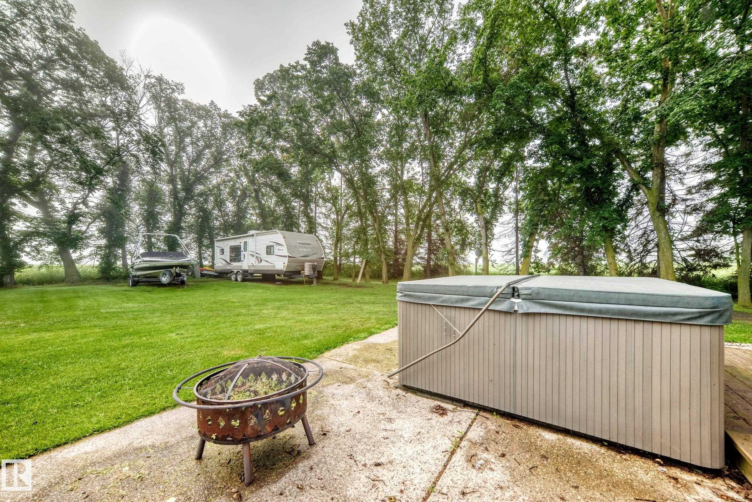 Expansive green lawn surrounded by mature trees, featuring a concrete patio with a fire pit and a covered hot tub - #38 24512 Sturgeon Rd, Rural Sturgeon County, AB