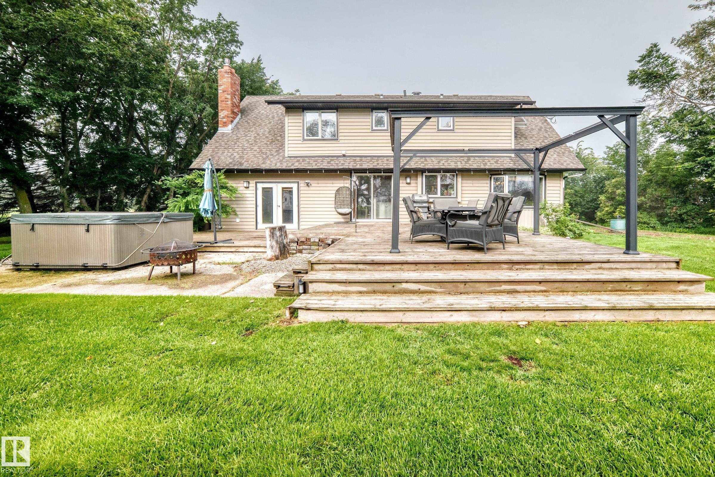 Expansive backyard featuring a composite wood deck with multiple steps, a hot tub, and a pergola structure - #38 24512 Sturgeon Rd, Rural Sturgeon County, AB