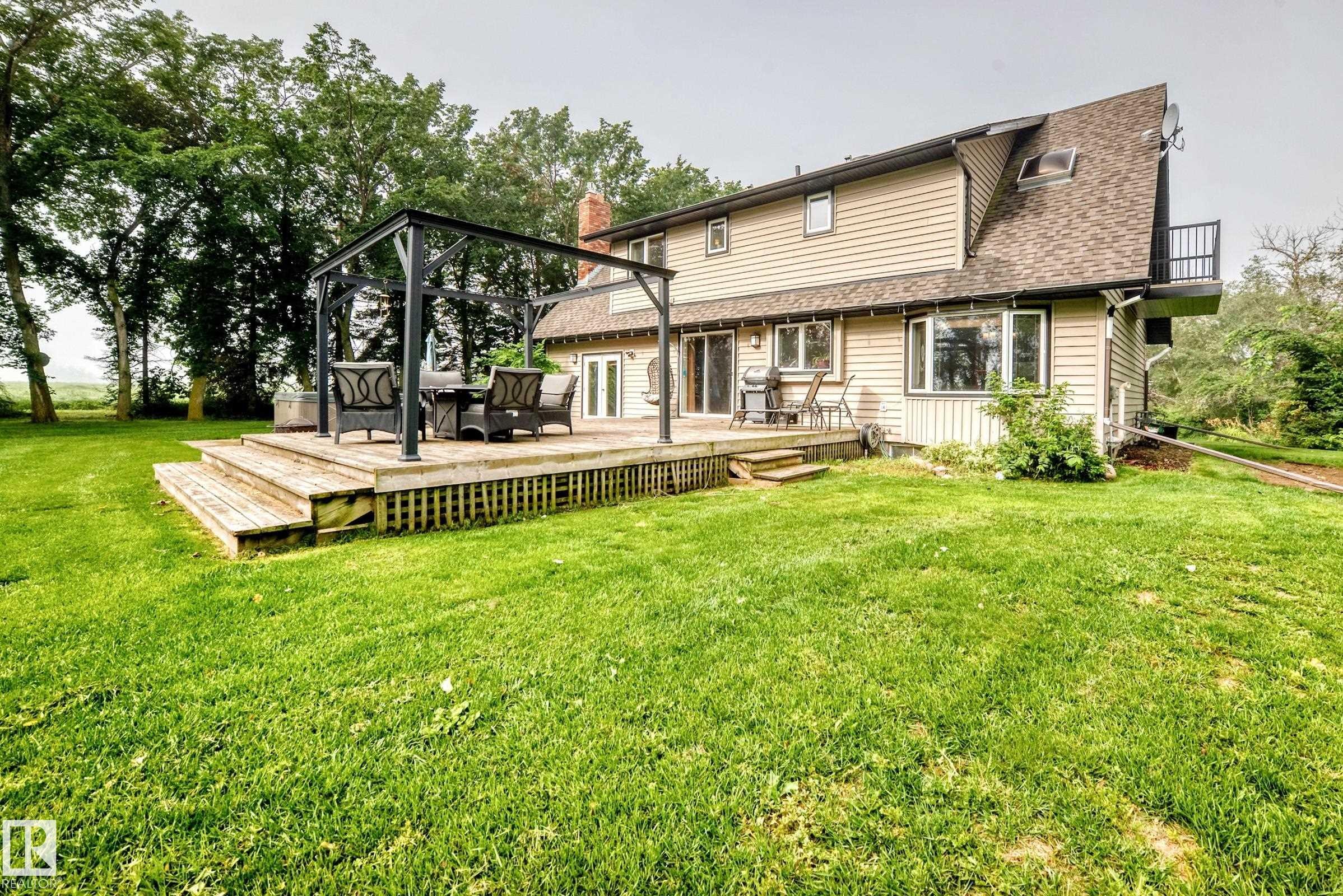 Expansive lawn with a multi-level wood deck, a patio door, and a second-story balcony - #38 24512 Sturgeon Rd, Rural Sturgeon County, AB