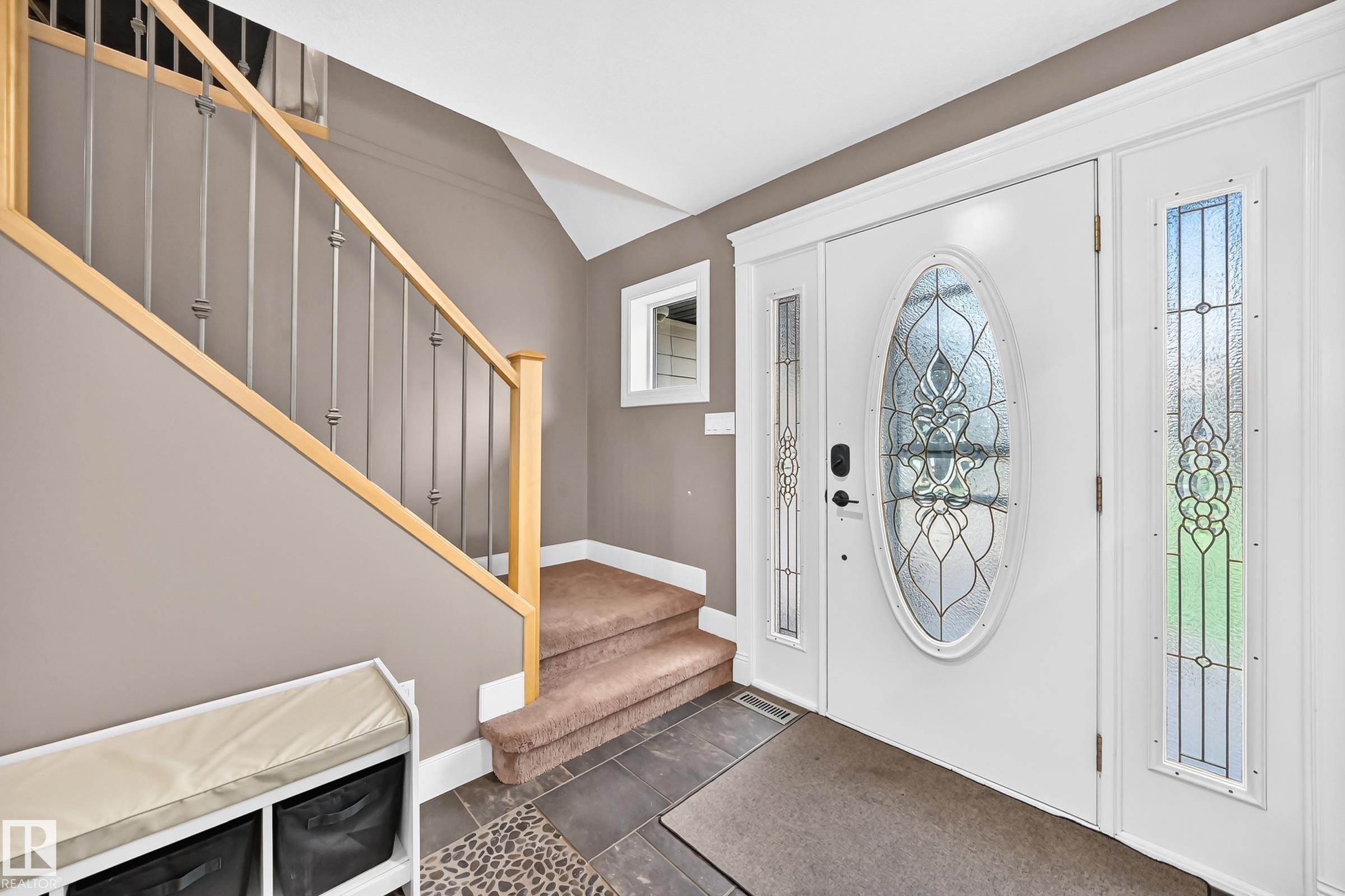 Entryway featuring a white door with decorative oval glass insert, two sidelight windows with patterned glass, and a staircase with light wood handrails and dark metal balusters - #38 24512 Sturgeon Rd, Rural Sturgeon County, AB