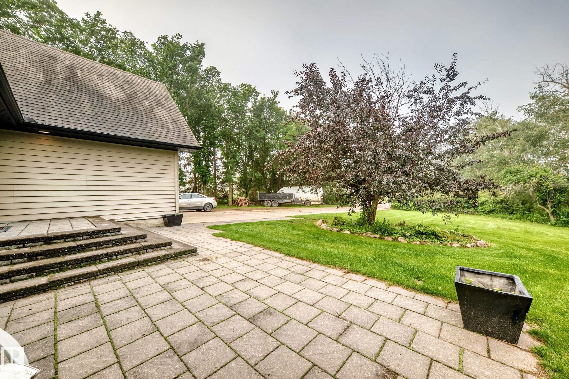 Expansive paved patio with stone steps, mature tree, and lush green lawn - #38 24512 Sturgeon Rd, Rural Sturgeon County, AB