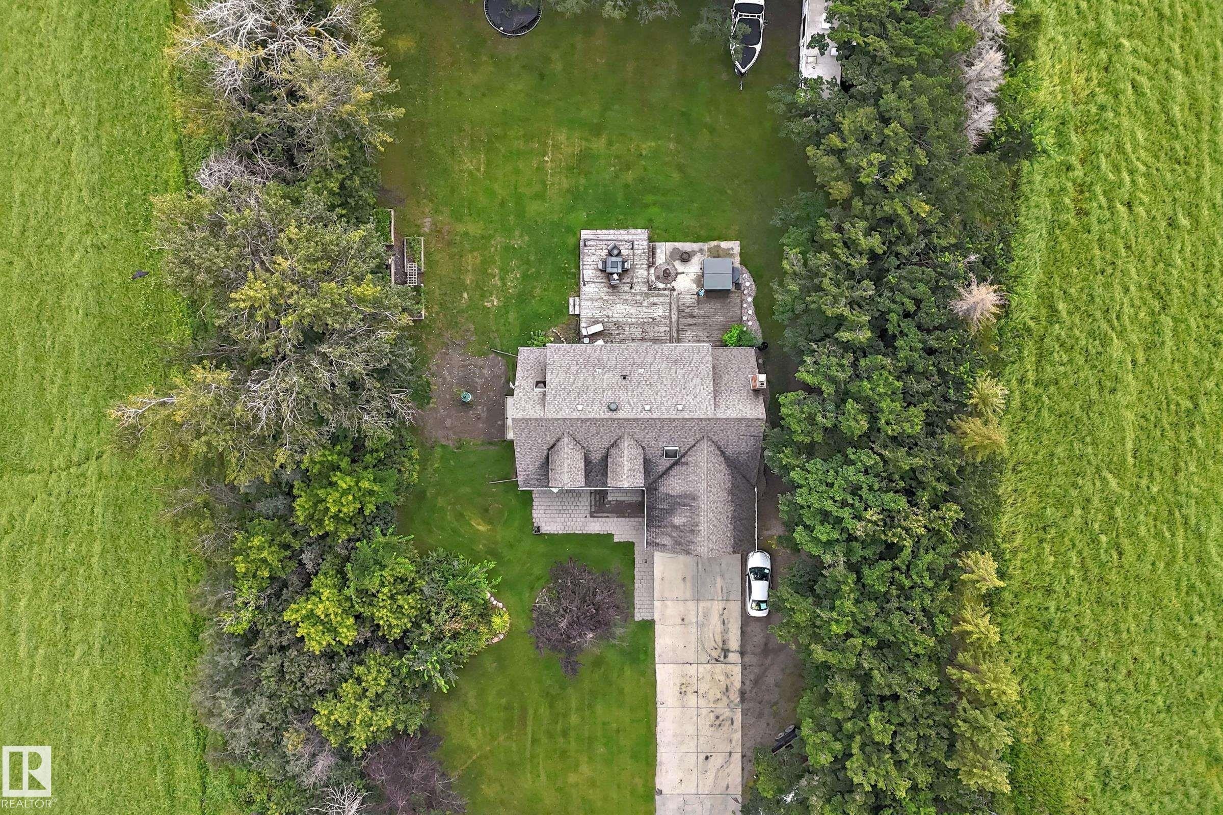 Spacious property featuring expansive green lawns, mature perimeter trees, a multi-gabled roofline, a concrete driveway, and an outdoor patio with hardscaping - #38 24512 Sturgeon Rd, Rural Sturgeon County, AB