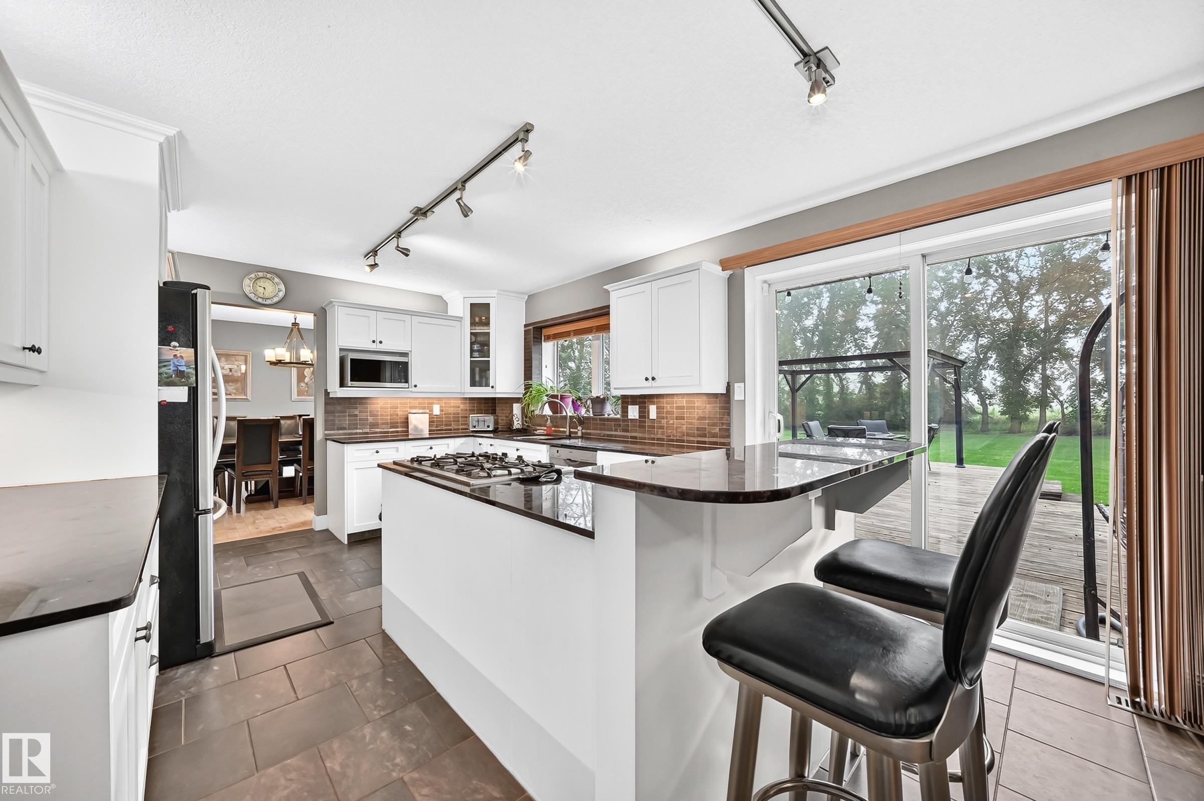 Kitchen featuring white cabinetry, dark countertops, a built-in microwave, and a gas stovetop on the island - #38 24512 Sturgeon Rd, Rural Sturgeon County, AB