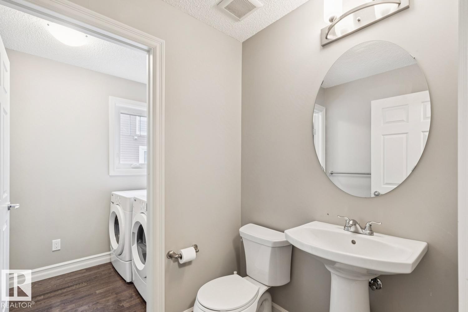 Pedestal sink with chrome fixtures, oval mirror, and overhead vanity lighting - 5409 3 Avenue Sw, Edmonton, AB - Indoor