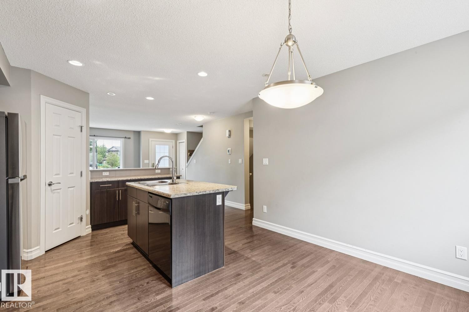 Kitchen island with built-in sink and dishwasher, wood-finish flooring, recessed lighting, and a contemporary pendant light fixture - 5409 3 Avenue Sw, Edmonton, AB - Indoor Photo Showing Kitchen