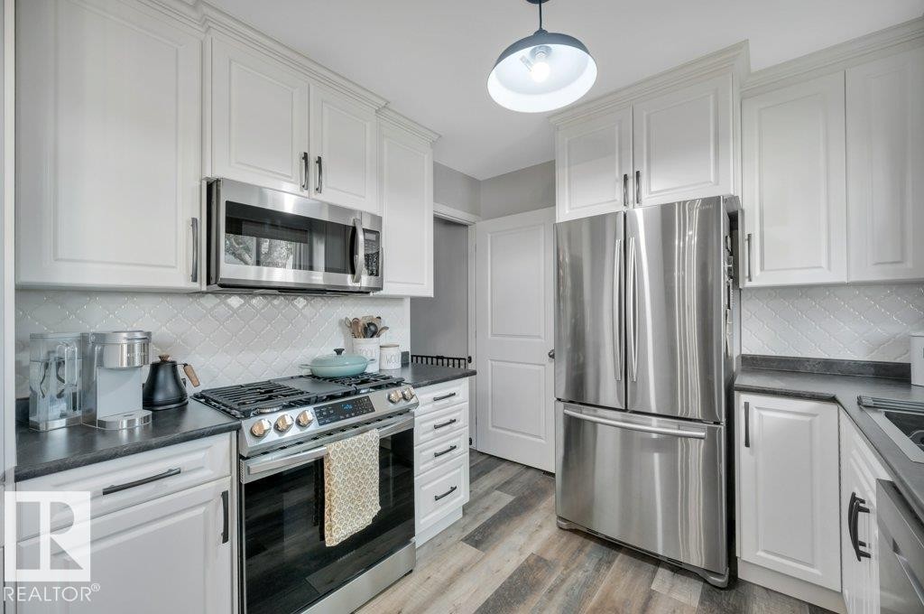 White shaker cabinetry, stainless steel appliances, dark countertops, patterned tile backsplash, and vinyl plank flooring - #138 5231 51 St, Bon Accord, AB - Indoor Photo Showing Kitchen With Upgraded Kitchen