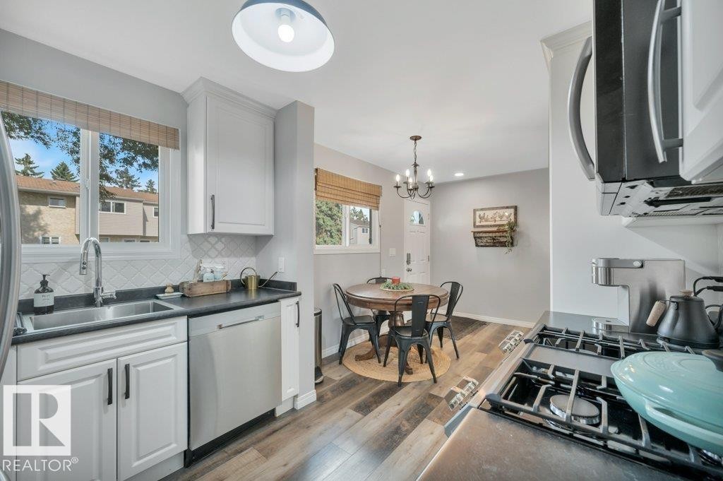 White cabinetry with dark hardware, stainless steel appliances, dark countertops, vinyl plank flooring, and a white subway tile backsplash - #138 5231 51 St, Bon Accord, AB - Indoor Photo Showing Kitchen