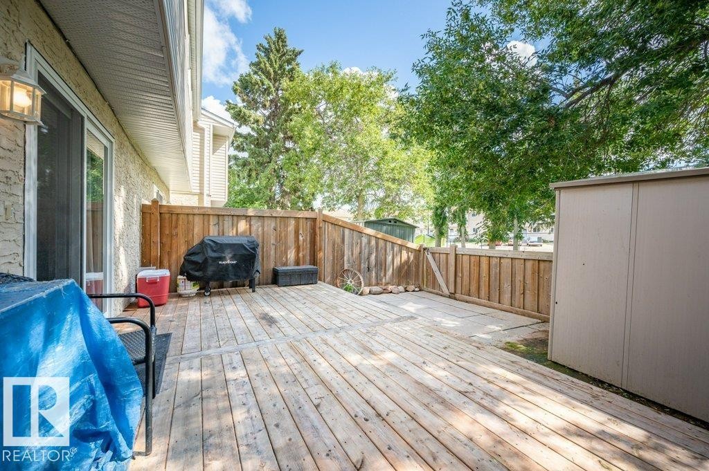 Expansive wood deck with a built-in privacy fence, featuring a sliding glass door entry and an exterior light fixture - #138 5231 51 St, Bon Accord, AB - Outdoor With Deck Patio Veranda With Exterior