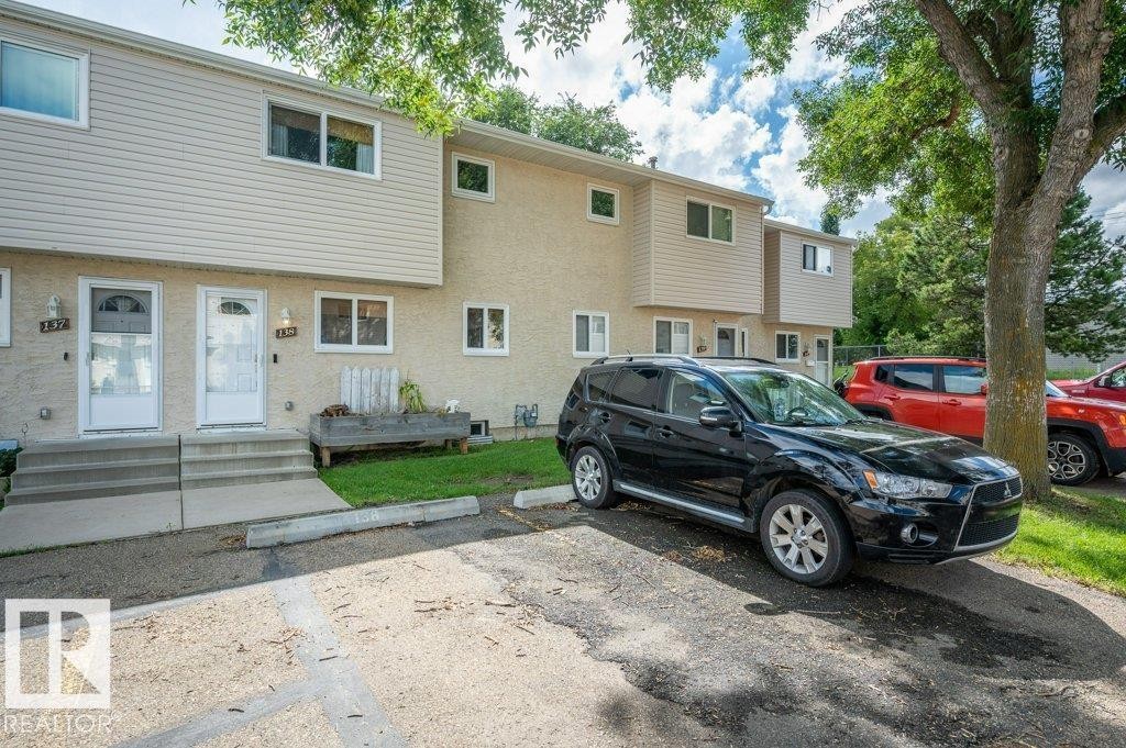 Townhouse-style multi-unit building with light-colored siding and stucco exterior, individual entry doors, and concrete steps - #138 5231 51 St, Bon Accord, AB - Outdoor