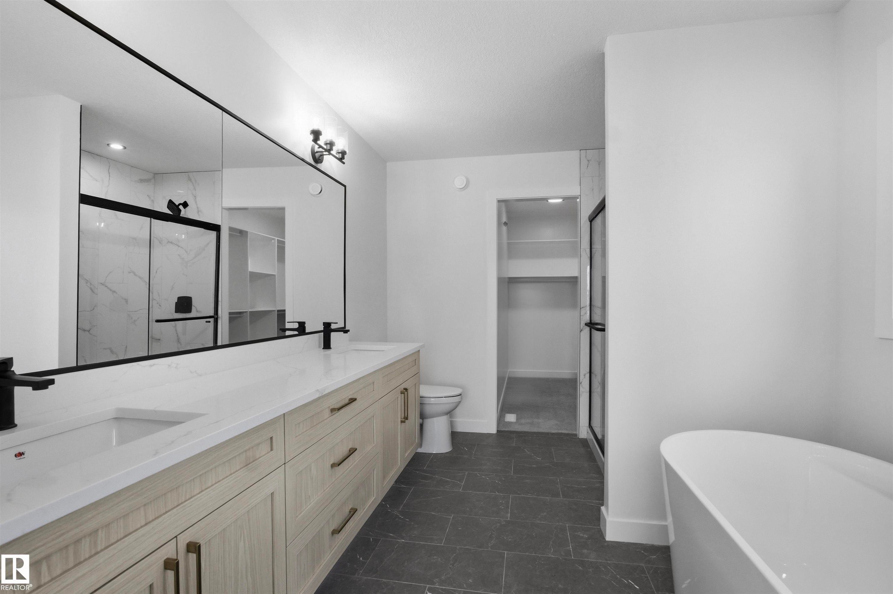 Dual vanity with integrated sinks, light wood-finish cabinetry, a large frameless mirror, and matte black fixtures - 3304 Chickadee Drive Nw, Edmonton, AB - Indoor Photo Showing Bathroom