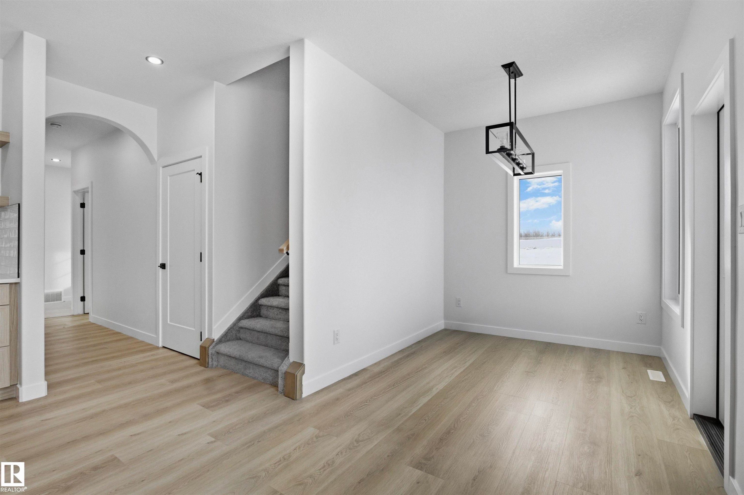 Recessed lighting, wood-finish flooring, arched doorway, contemporary stairwell with carpeted treads, and a modern rectangular chandelier - 3304 Chickadee Drive Nw, Edmonton, AB - Indoor Photo Showing Other Room