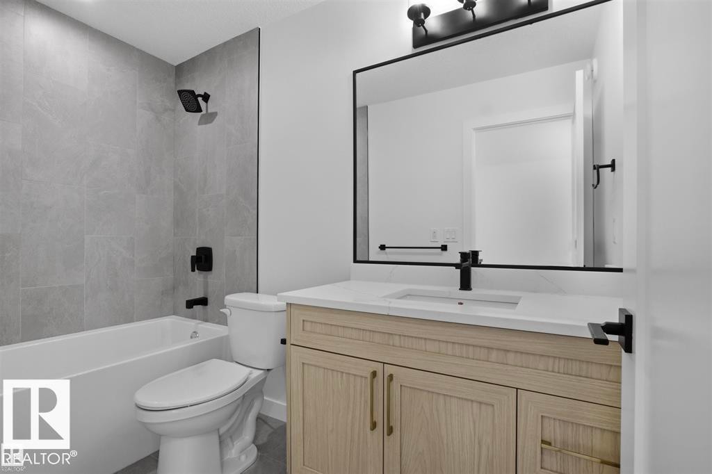 Neutral toned large format wall tiling, matte black fixtures, light wood-finish vanity, solid surface countertop, and integrated sink - 3304 Chickadee Drive Nw, Edmonton, AB - Indoor Photo Showing Bathroom