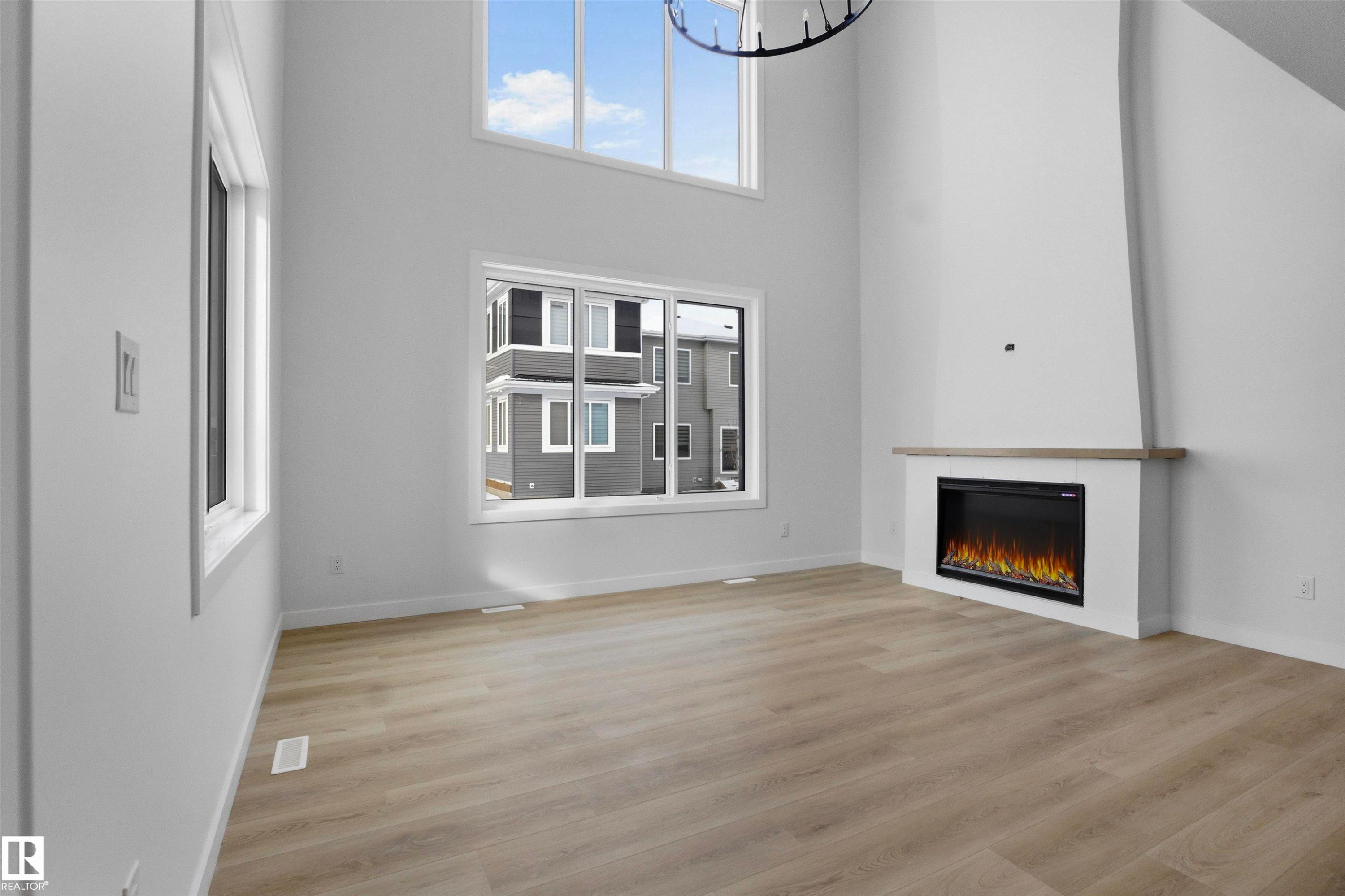 Vaulted ceiling with an upper window, wood-finish flooring, recessed electric fireplace with a mantel, and bright white walls - 3304 Chickadee Drive Nw, Edmonton, AB - Indoor Photo Showing Other Room With Fireplace