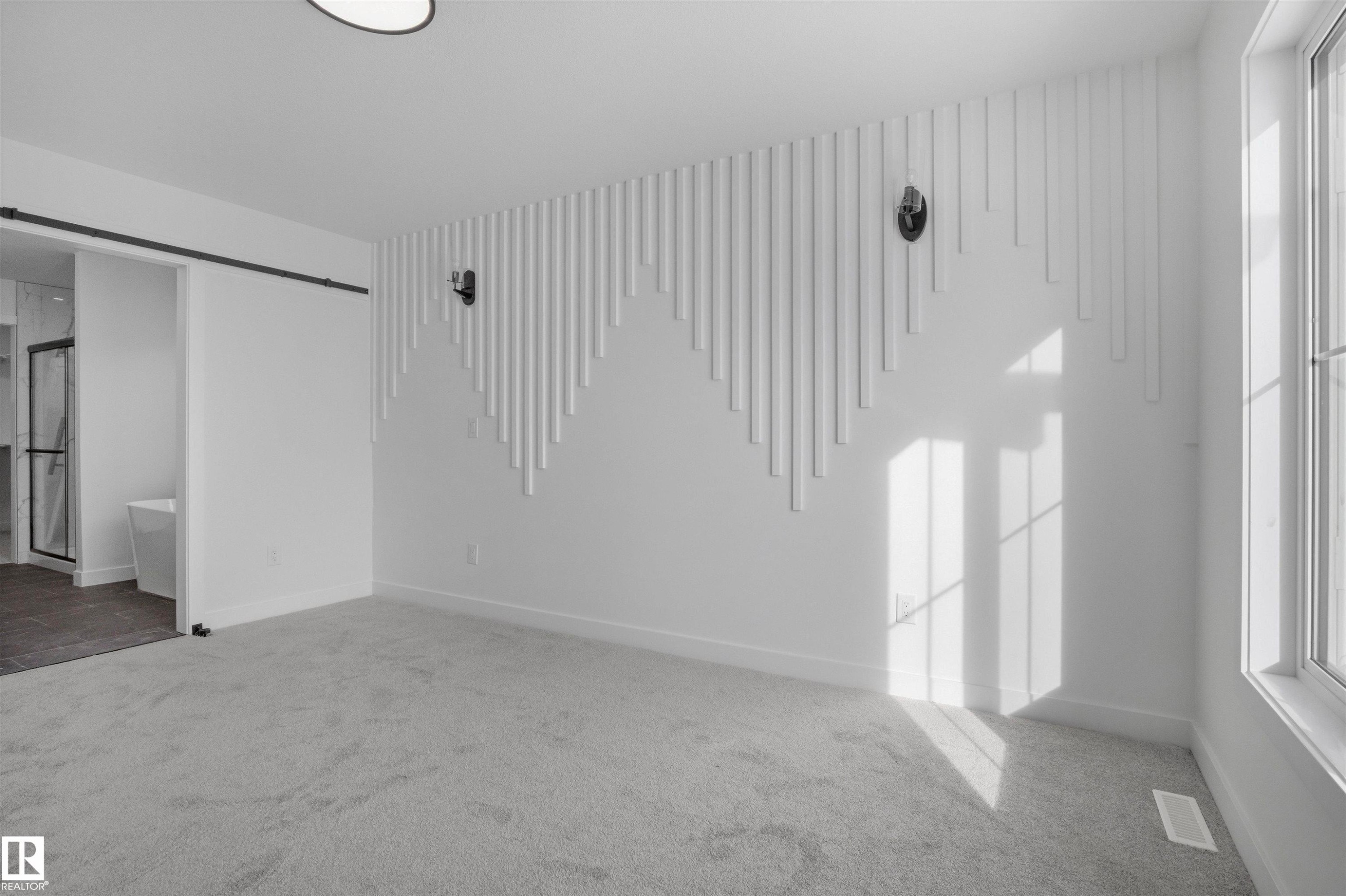 Patterned accent wall with integrated sconce lighting, large window, ceiling-mounted light fixture, and light-toned carpeting - 3304 Chickadee Drive Nw, Edmonton, AB - Indoor Photo Showing Other Room