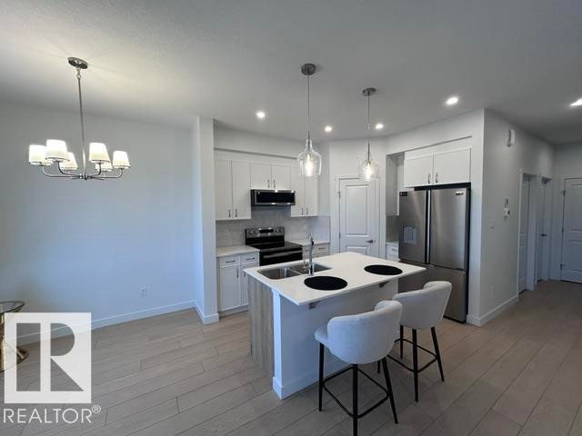 Modern kitchen featuring stainless steel appliances, white cabinetry, a central island with seating, and pendant lighting - 20936 16 Avenue Nw, Edmonton, AB - Indoor