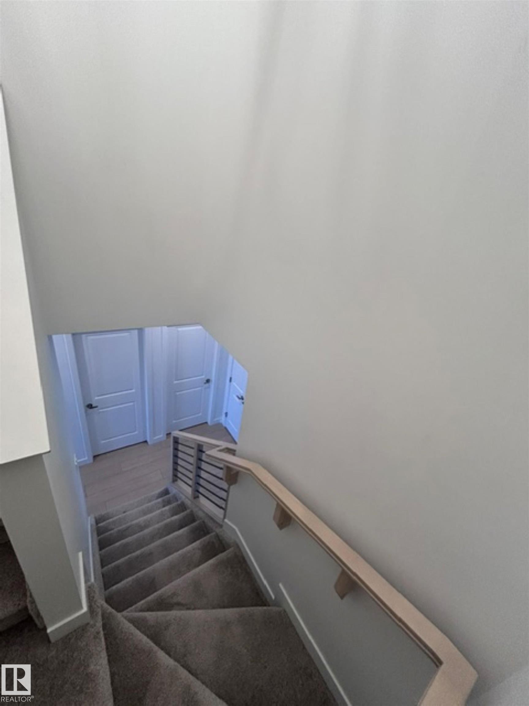 Carpeted staircase with light wood-finish handrail, horizontal metal balusters, and white interior doors - 20936 16 Avenue Nw, Edmonton, AB - Indoor Photo Showing Other Room