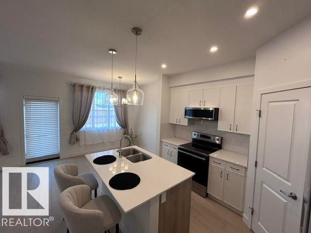 Kitchen featuring a central island with dual sinks, white cabinetry, integrated stainless steel appliances, and recessed lighting - 20936 16 Avenue Nw, Edmonton, AB - Indoor Photo Showing Kitchen With Double Sink