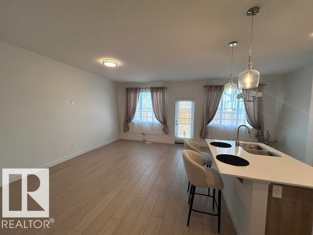 Open-concept living space featuring wood-finish flooring, a kitchen island with integrated sink, pendant lighting, and an exterior door - 20936 16 Avenue Nw, Edmonton, AB - Indoor