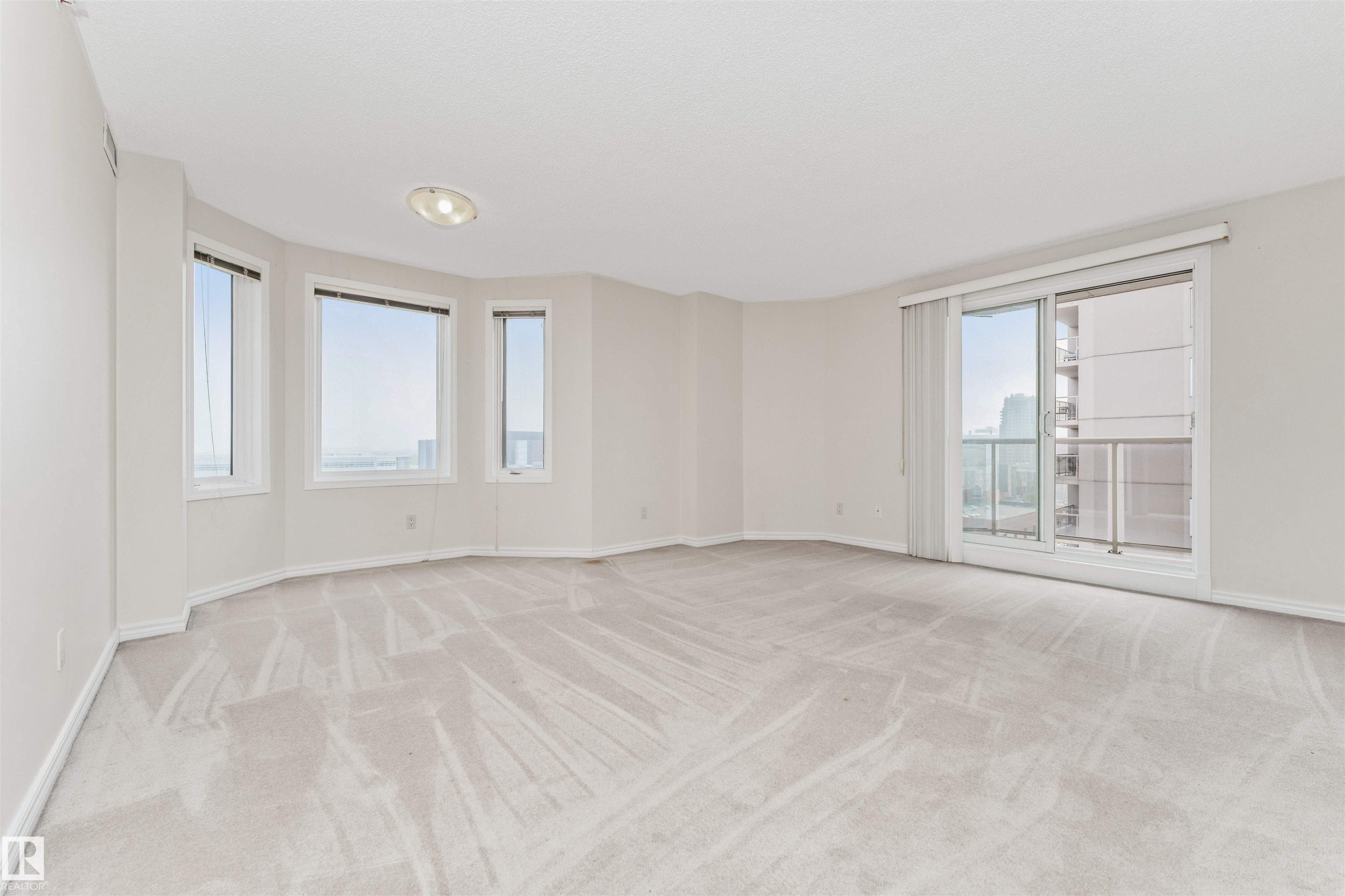 Expansive room with neutral carpeting, multiple windows providing natural light, and a sliding glass door leading to a balcony - #1101 10909 103 Av Nw, Edmonton, AB - Indoor Photo Showing Other Room